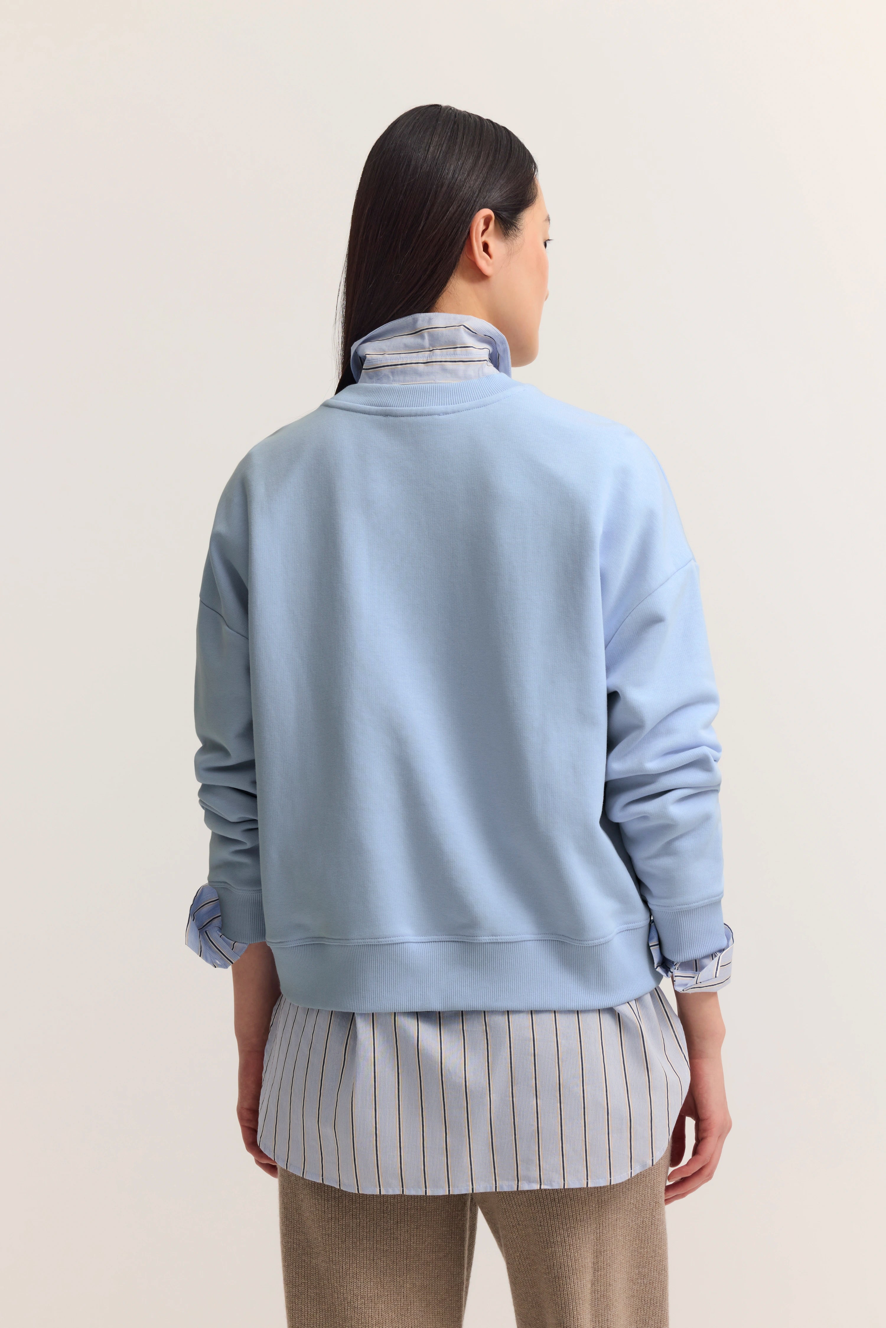 Rückansicht Model in hellblauem Pullover, gestreiftem Hemd und beige Hose, legerer Stil.
