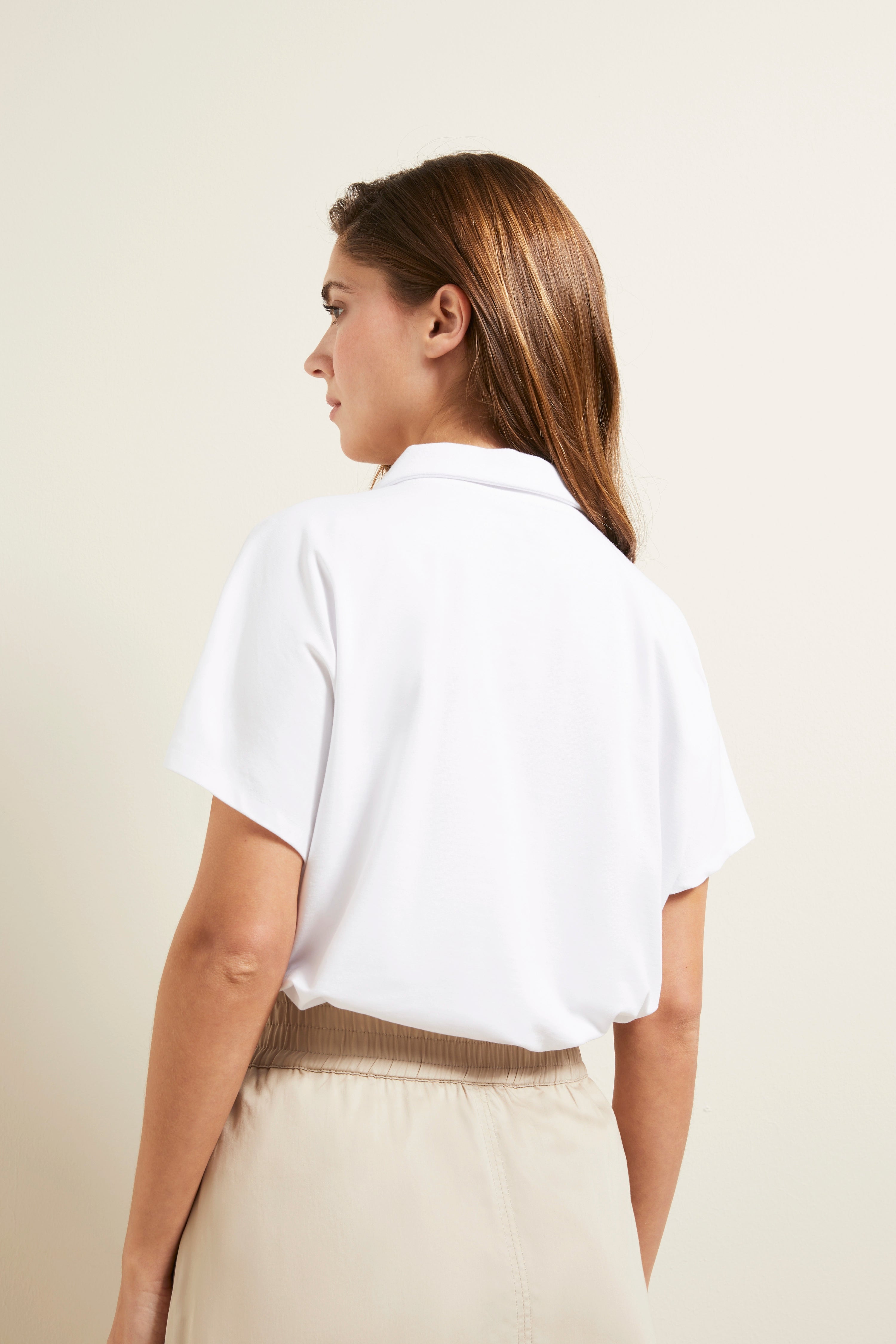 Weiße Bluse und beige Rock, Rückansicht, legeres Modelbild, entspannt stehende Pose.