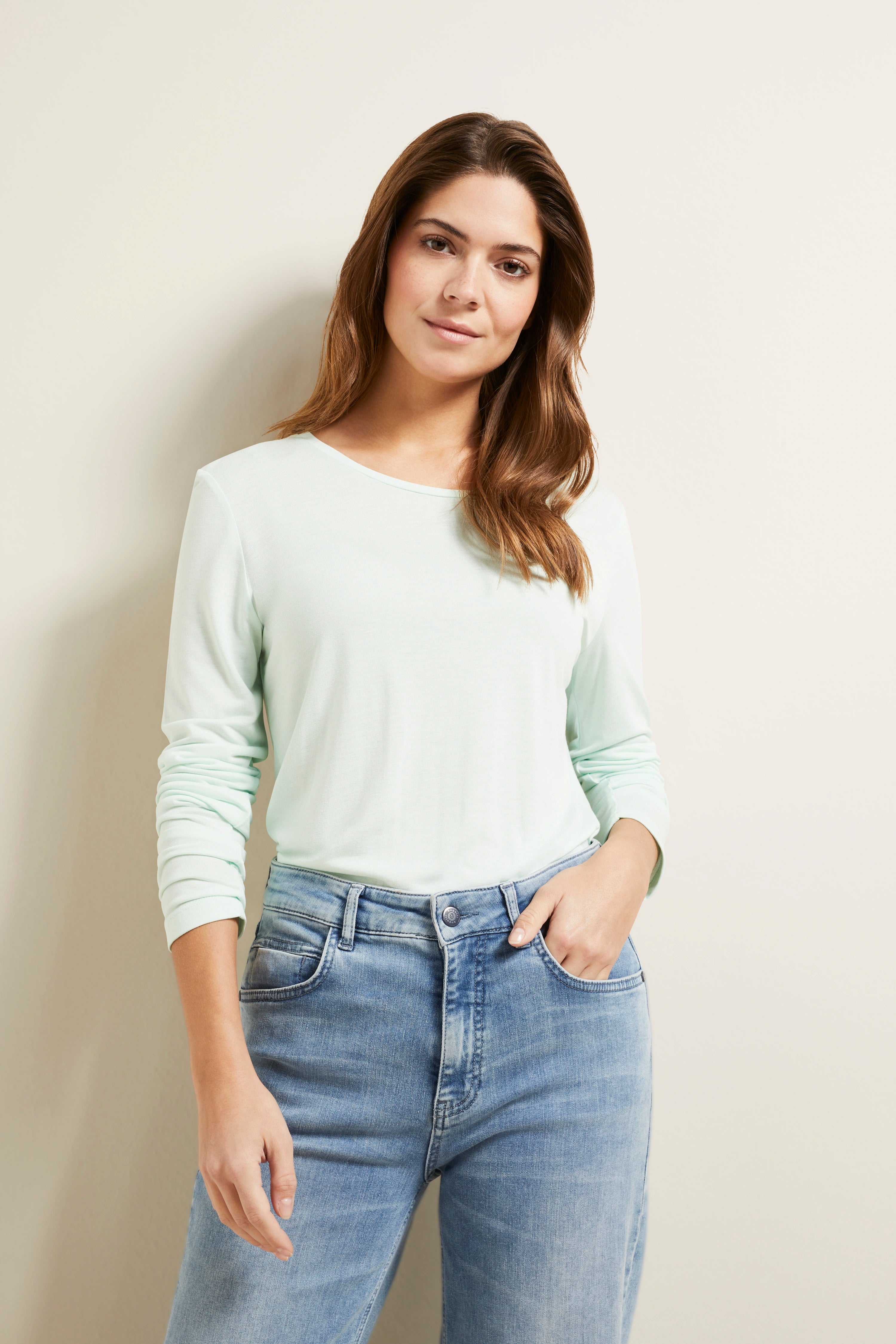 Model in mintgrünem Langarmshirt und blauer Jeans, locker lässige Pose, bugatti Stil.