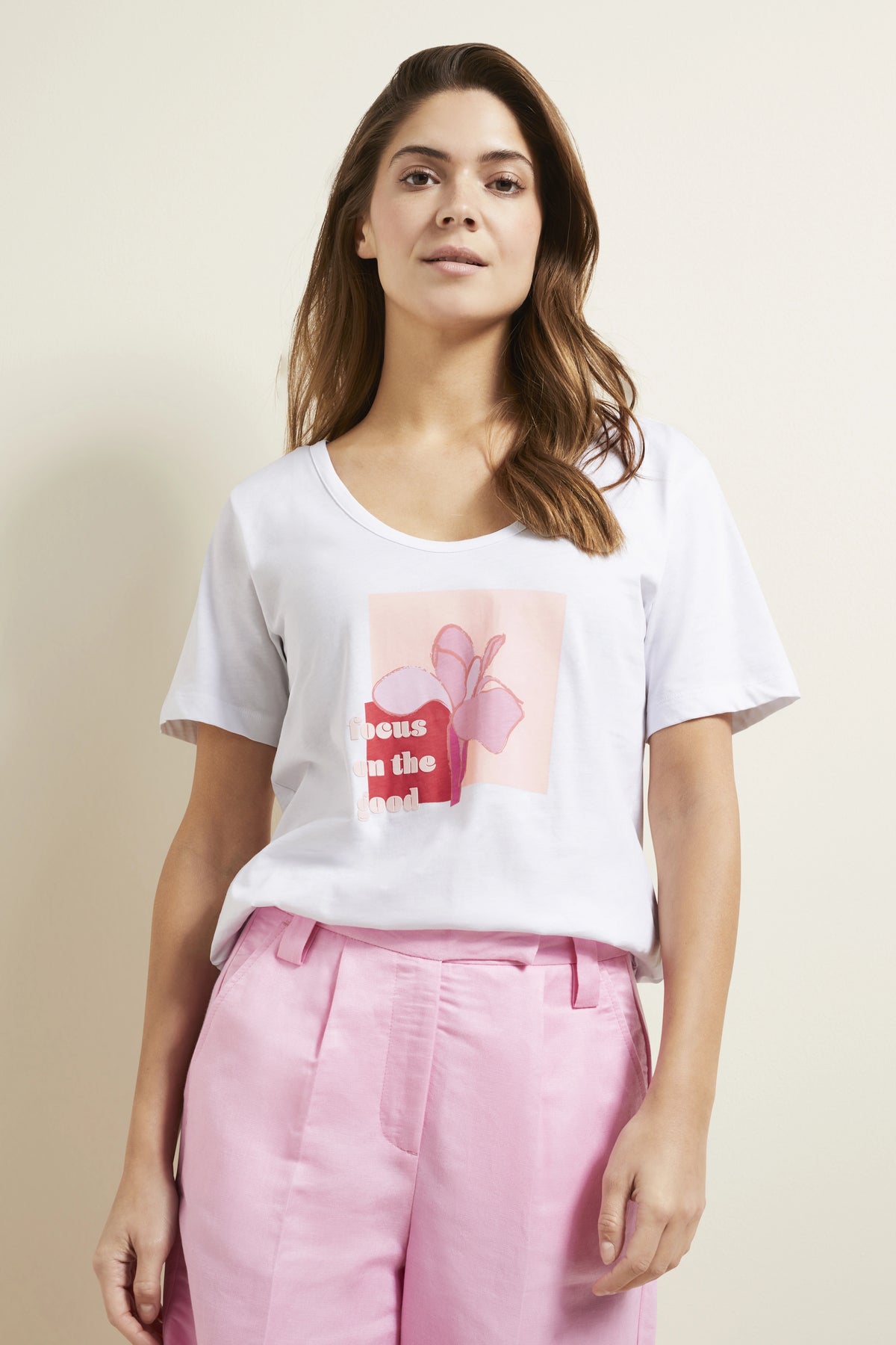 Weißes T-Shirt mit Grafik, rosa Shorts, Model lächelt sanft.