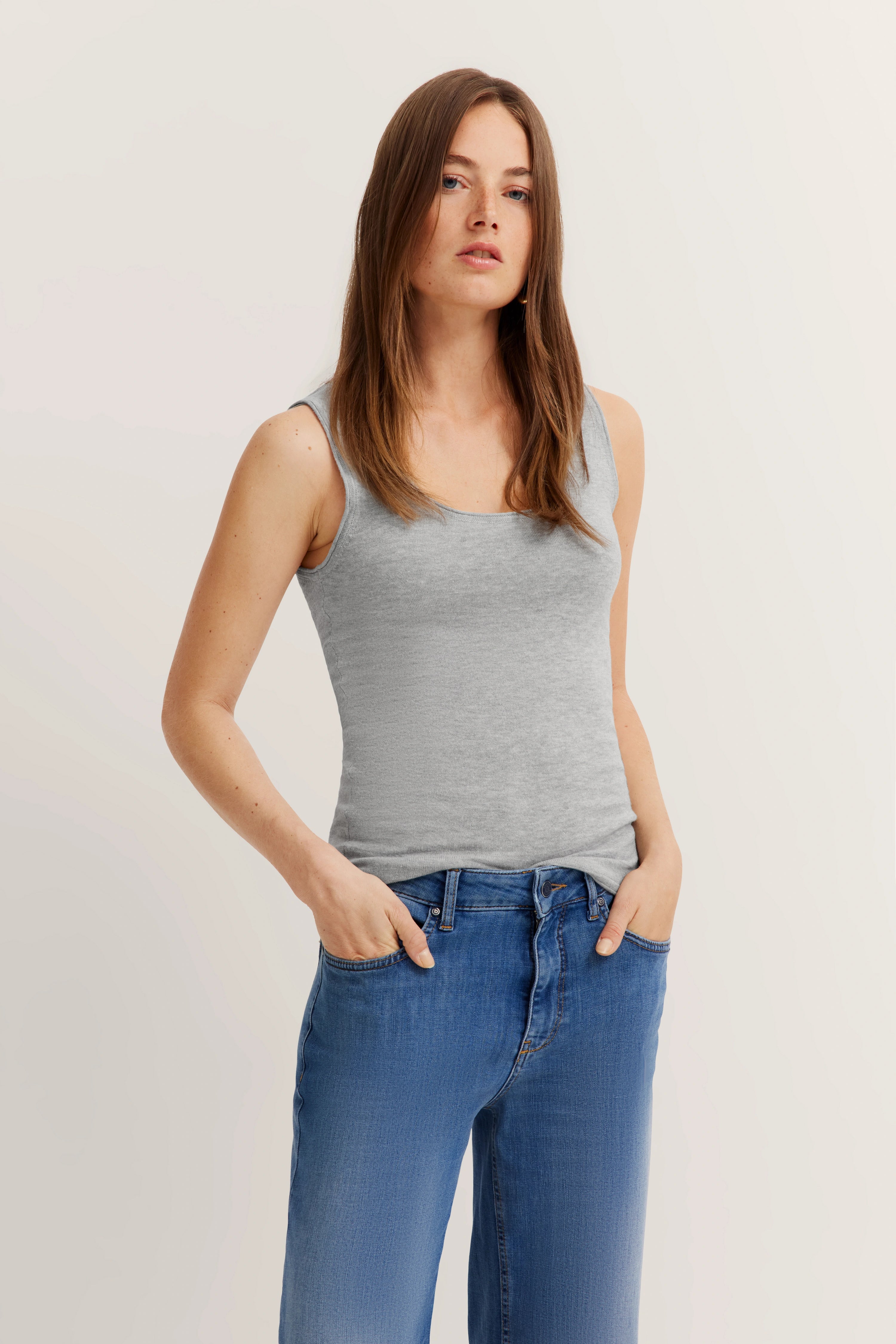 Graues Tanktop und blaue Jeans, legeres Modelbild, entspannte Haltung.