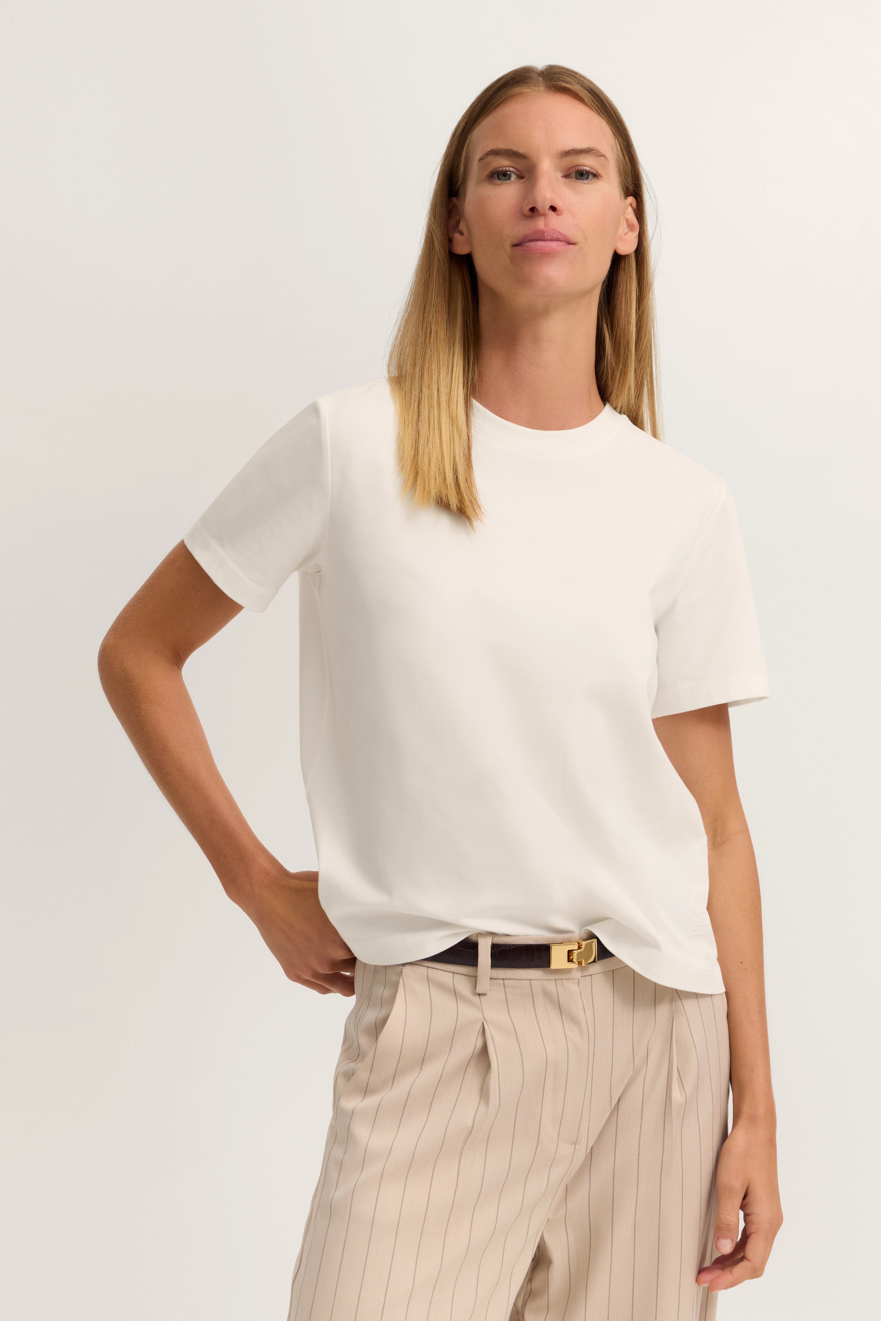 Weißes T-Shirt, beige gestreifte Hose, Modelbild, lässige Pose, Hand in der Hosentasche.