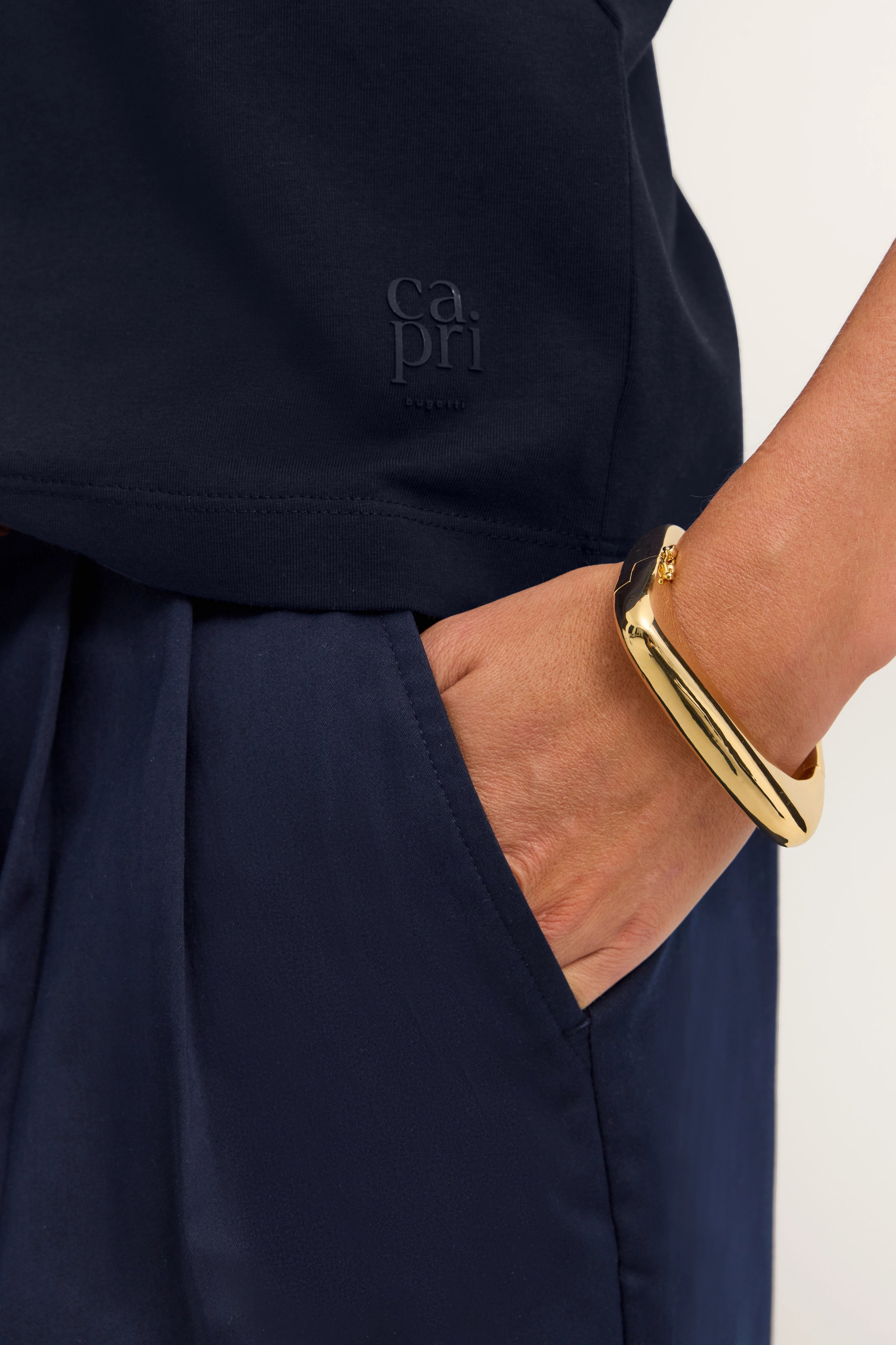 Navy Top mit Capri-Logo, goldenes Armband, Hand in Hosentasche, Detailansicht, bugatti Stil.