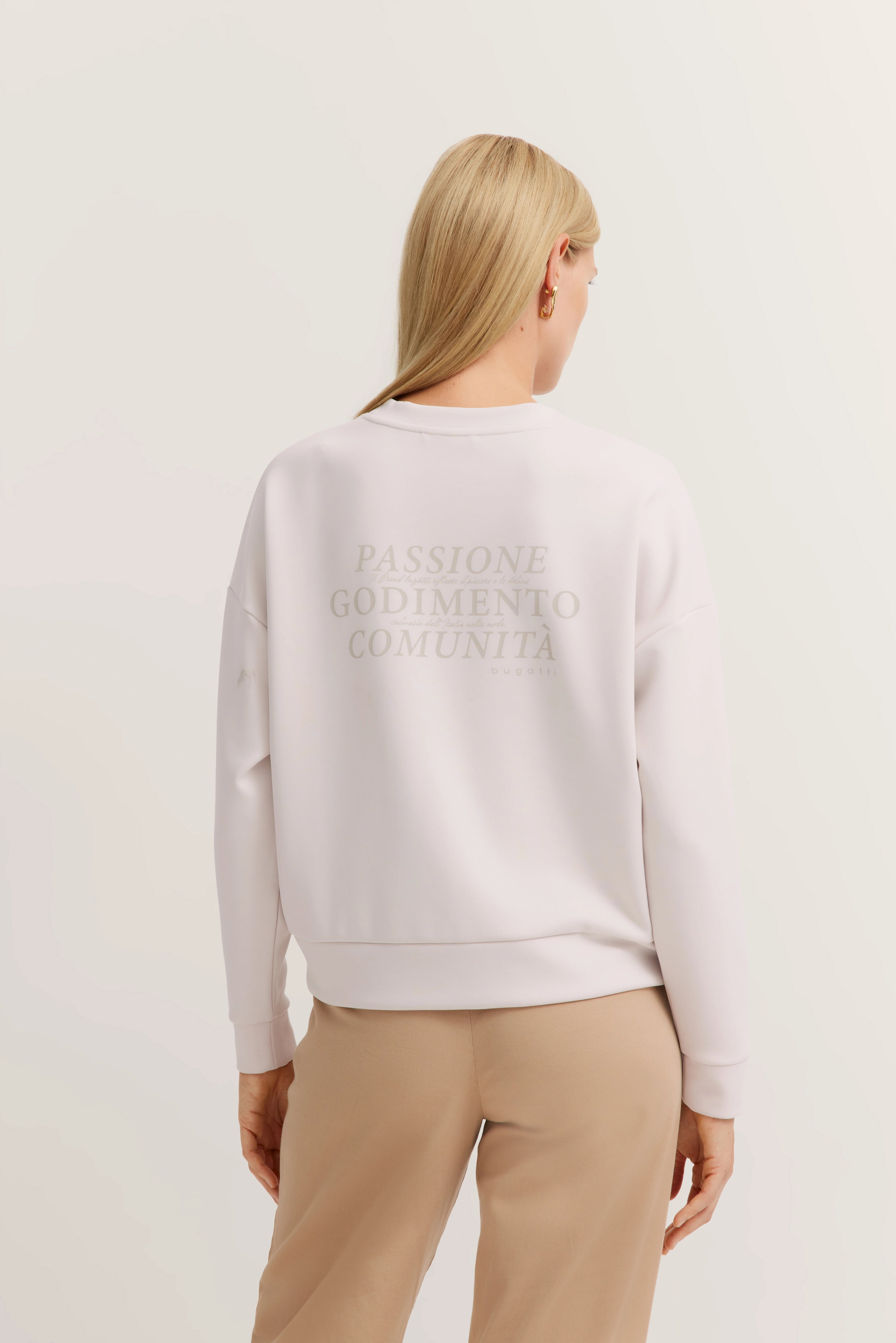 Model in weißem bugatti Sweatshirt mit Schriftzug, beige Hose, Rückansicht, entspannte Haltung.