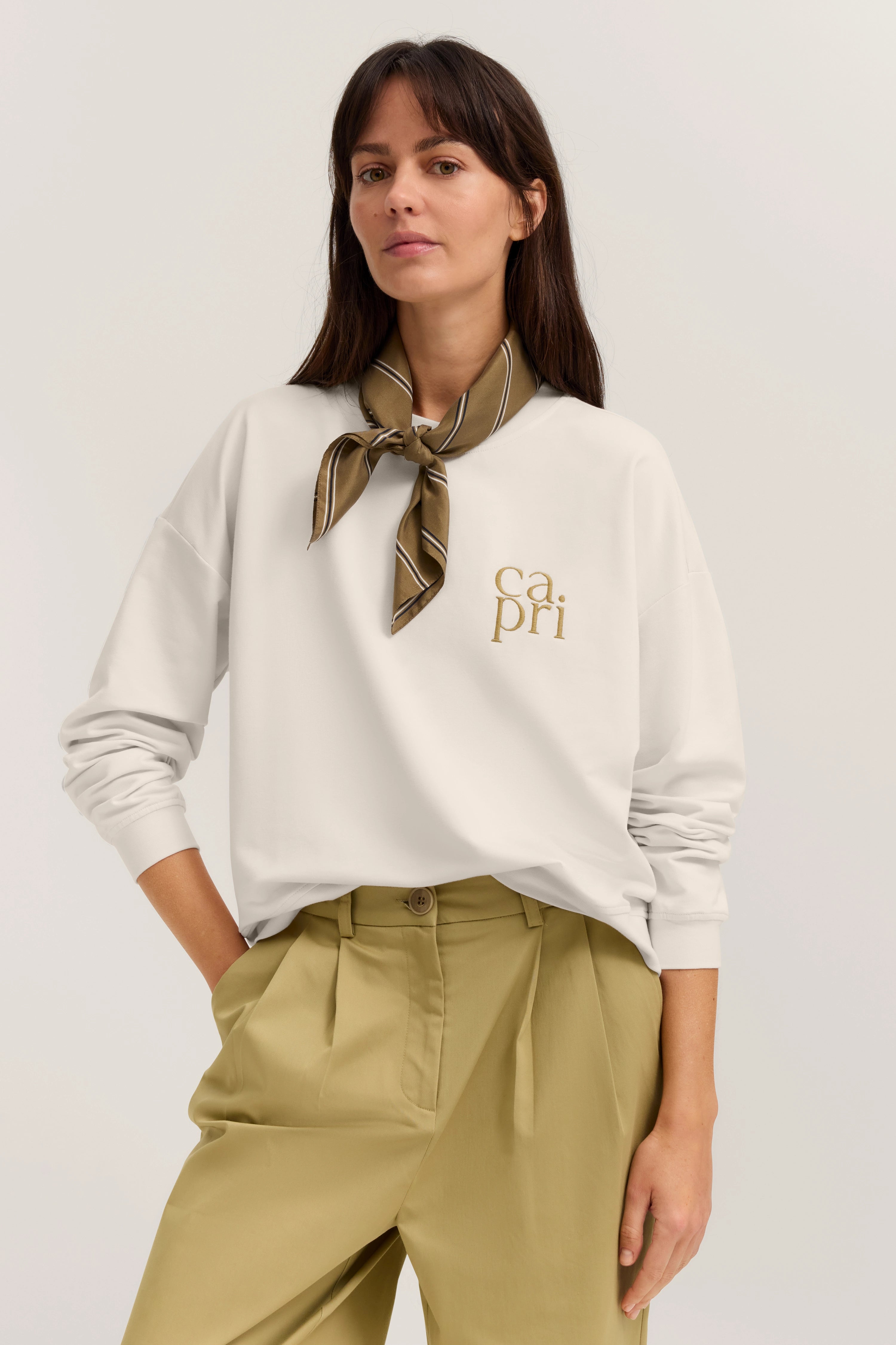 Weißer Pullover mit "capri" Schriftzug, olivgrüner Schal, beige Hose