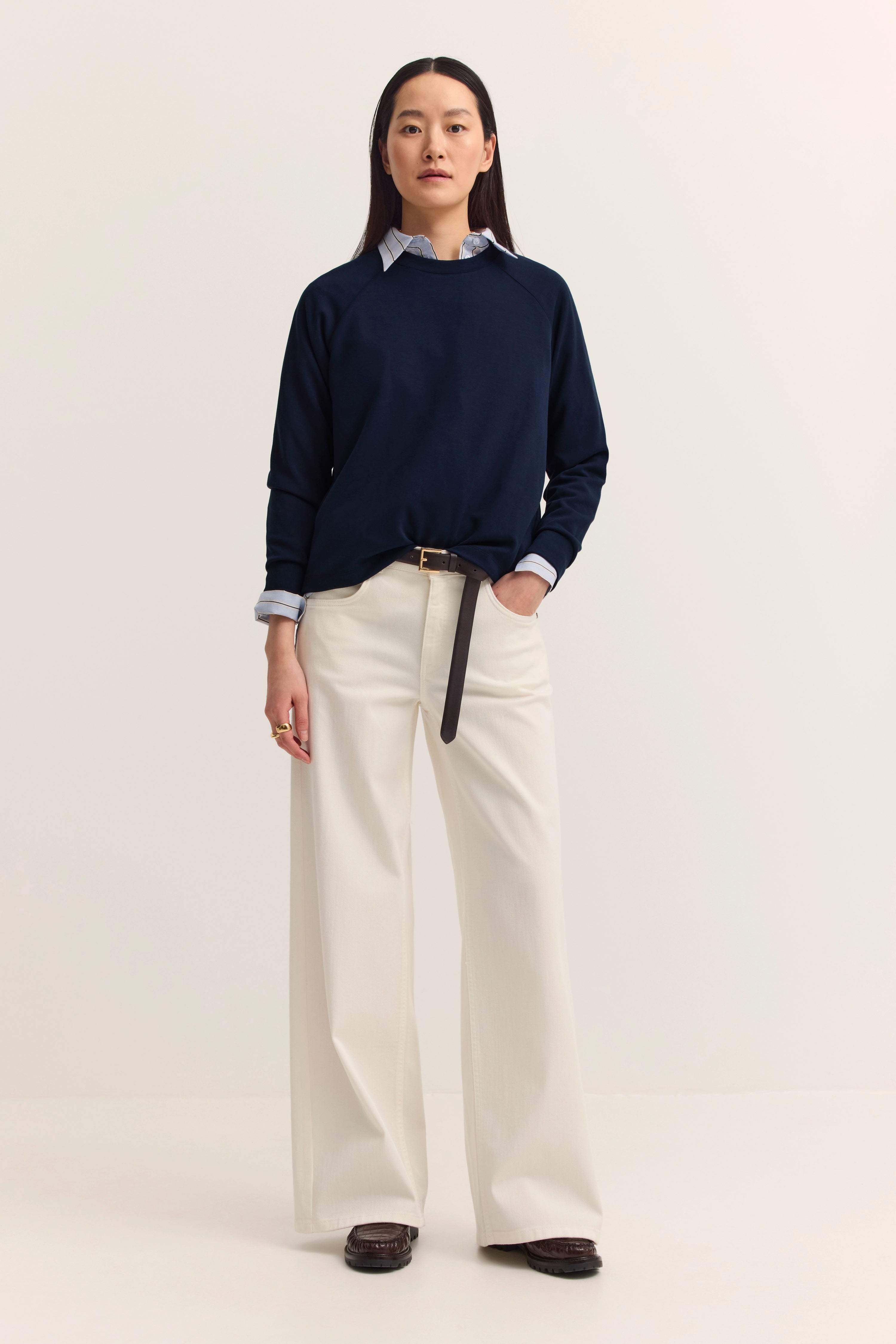 Model trägt dunkelblauen Pullover und weiße Hose, legeres Posing, bugatti Stil und Eleganz.