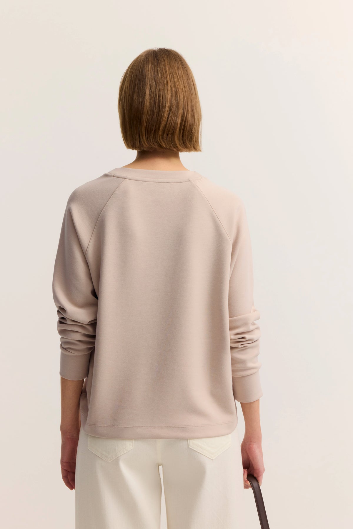 Beiger Pullover und weiße Hose, Rückansicht, legeres Modelbild, entspanntes Posing.