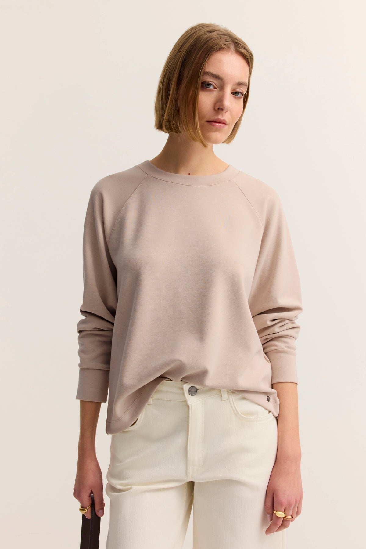 Beiges Sweatshirt, weiße Hose, Modelbild, entspannte Haltung.