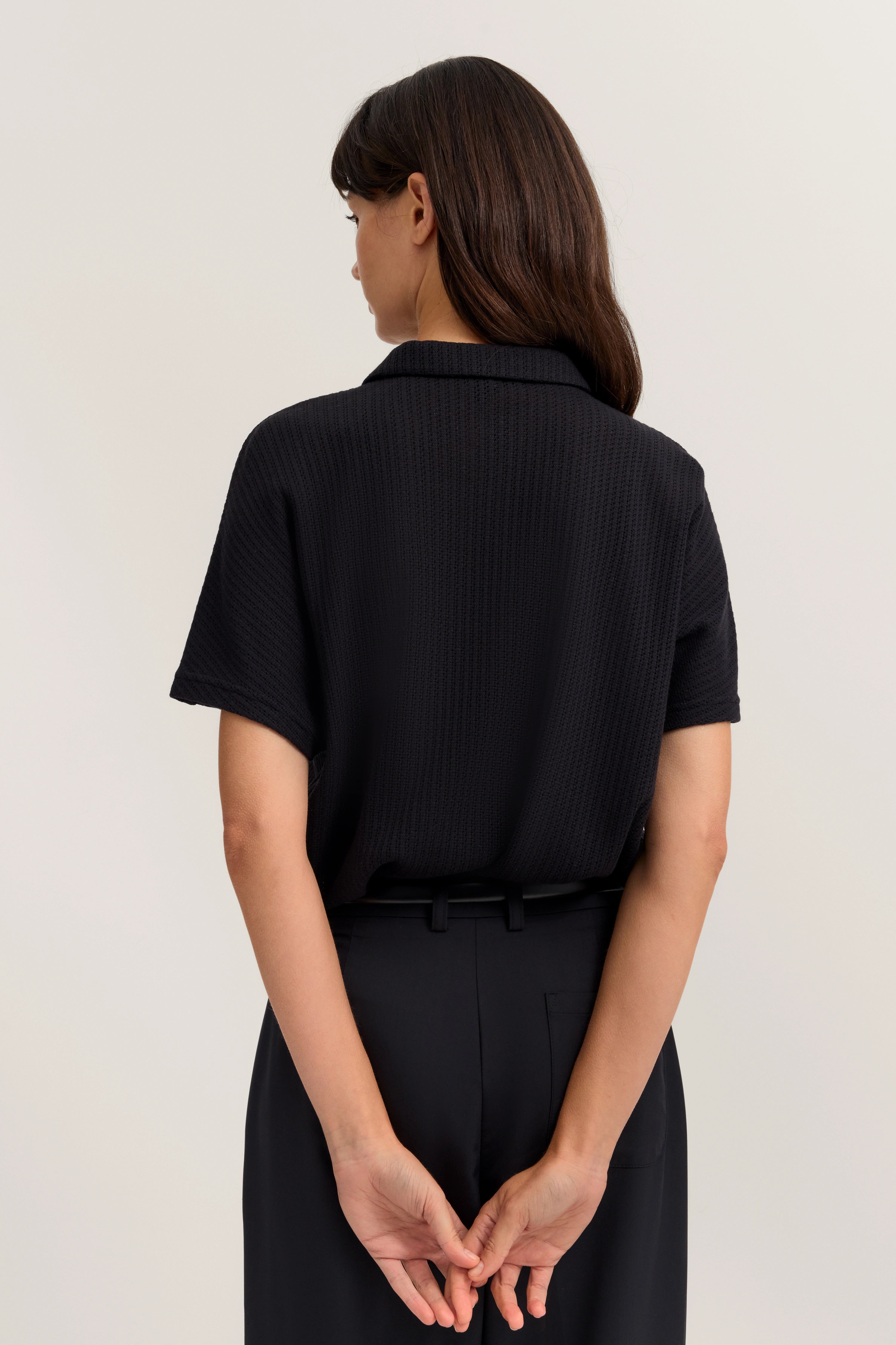 Schwarzes bugatti Outfit, Rückenansicht, Modelbild, lässige Pose mit verschränkten Händen.