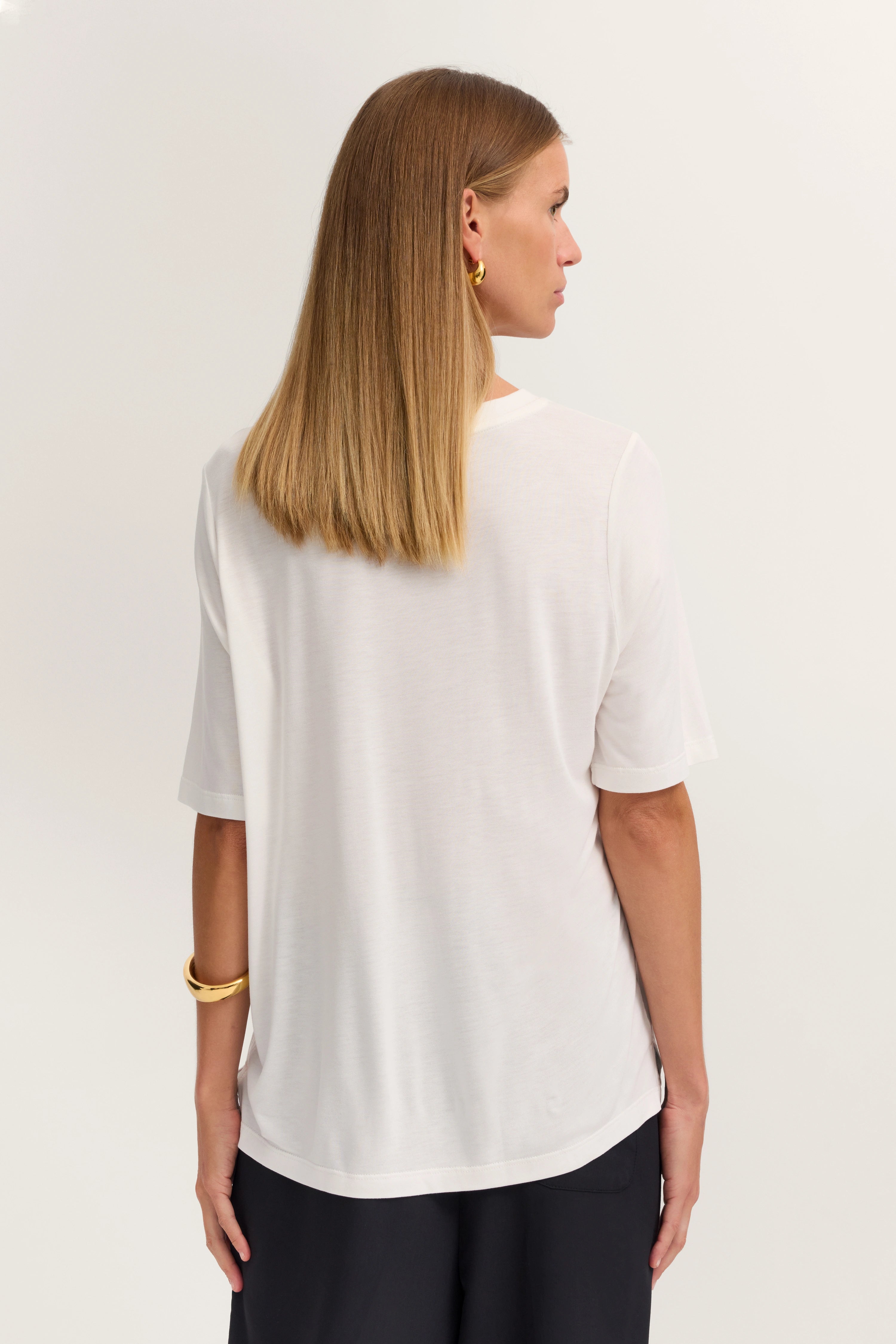 Weiße Bluse und schwarze Hose, Model von hinten, entspanntes Posing, bugatti Stil.