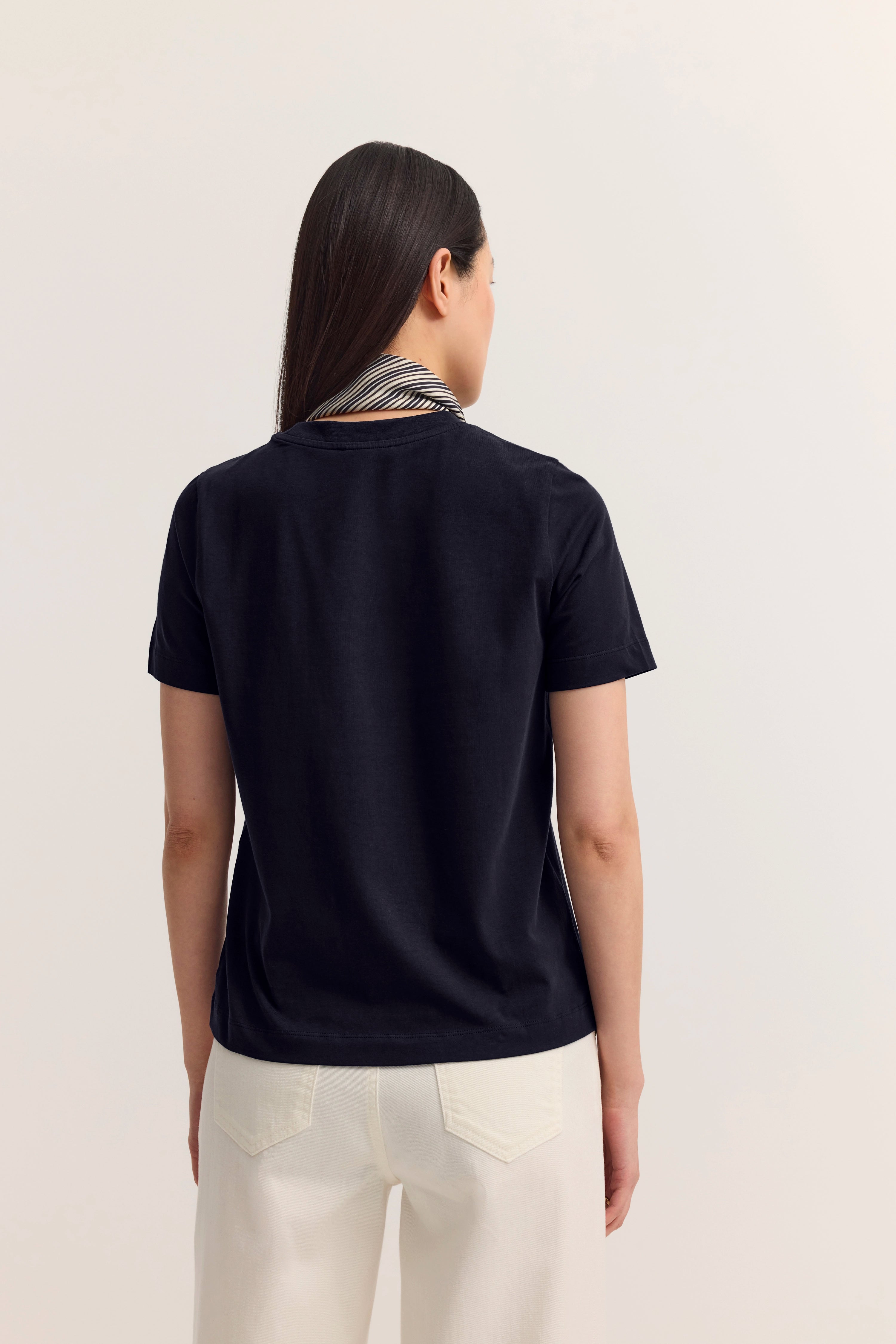 Schwarzes T-Shirt und weiße Hose, Model von hinten, lässige Pose, zeitloser Stil von bugatti.