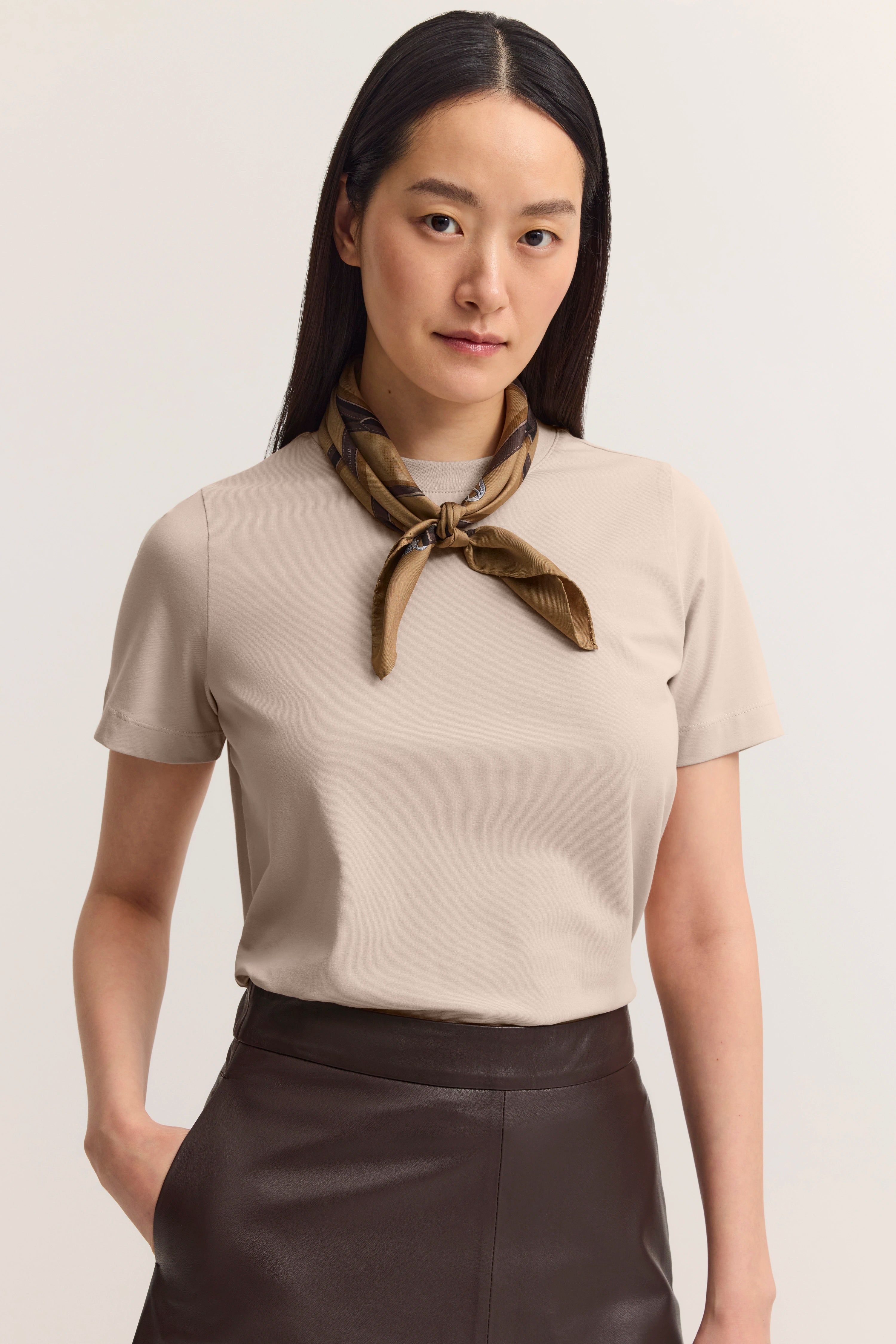 Modelbild: Frau in beigem Shirt, braunem Rock, mit braunem Schal. Entspanntes, stilvolles Posing.