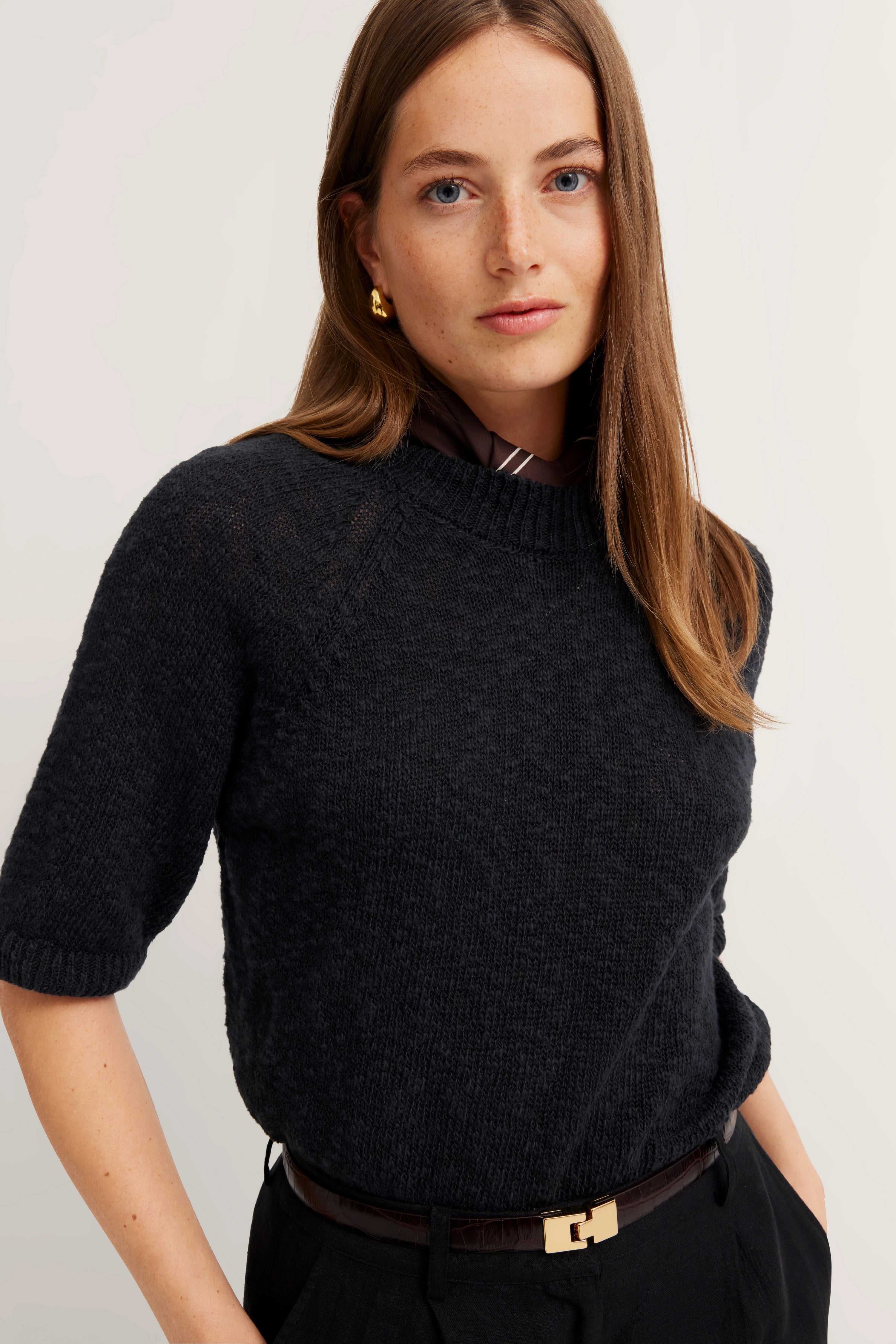 ALT: Model in schwarzem bugatti Pullover, legeres Portrait, entspannter Ausdruck, goldene Ohrringe.
