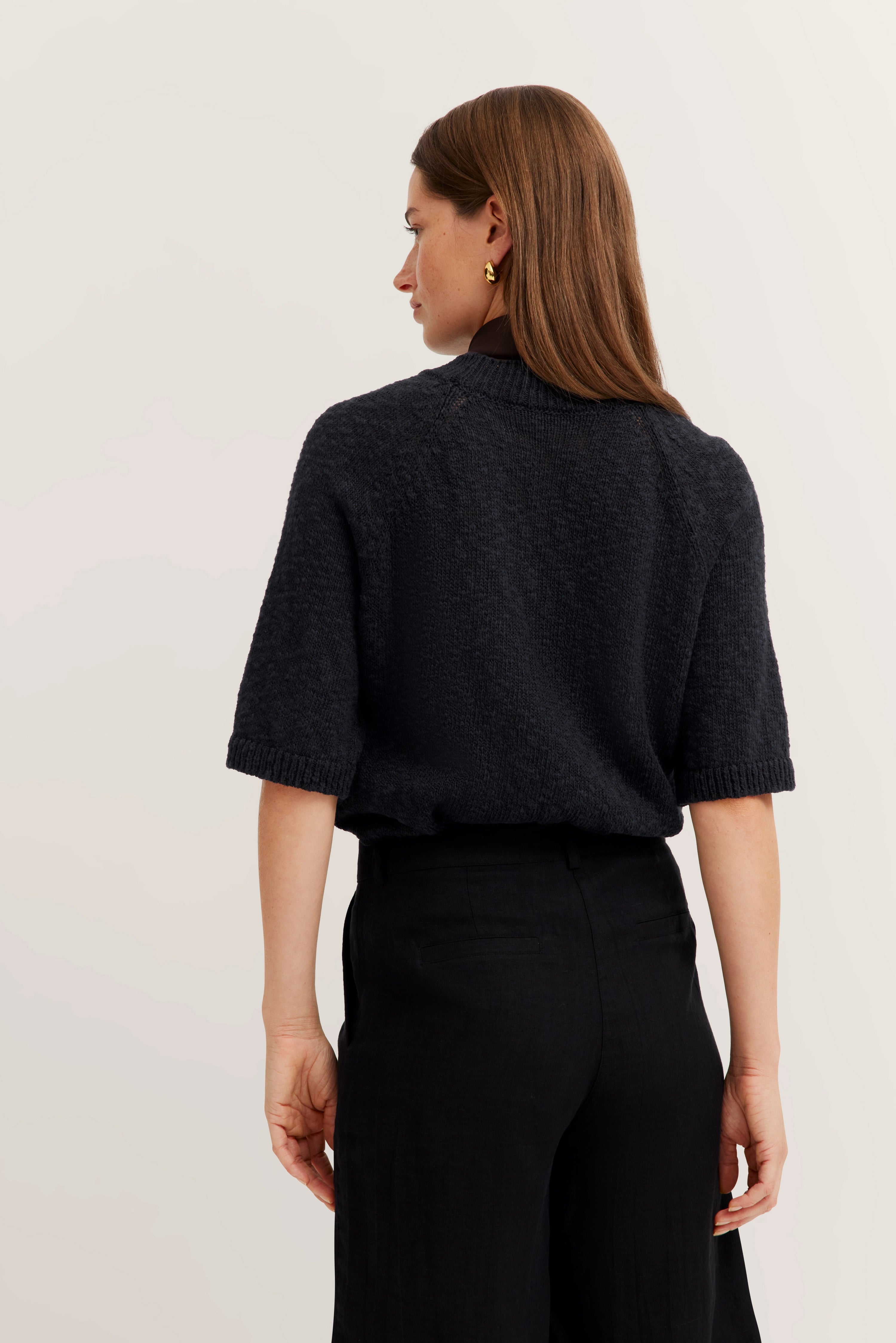 Schwarzes Strickoberteil, kurze Ärmel, Rückenansicht, Model mit entspanntem Posing.