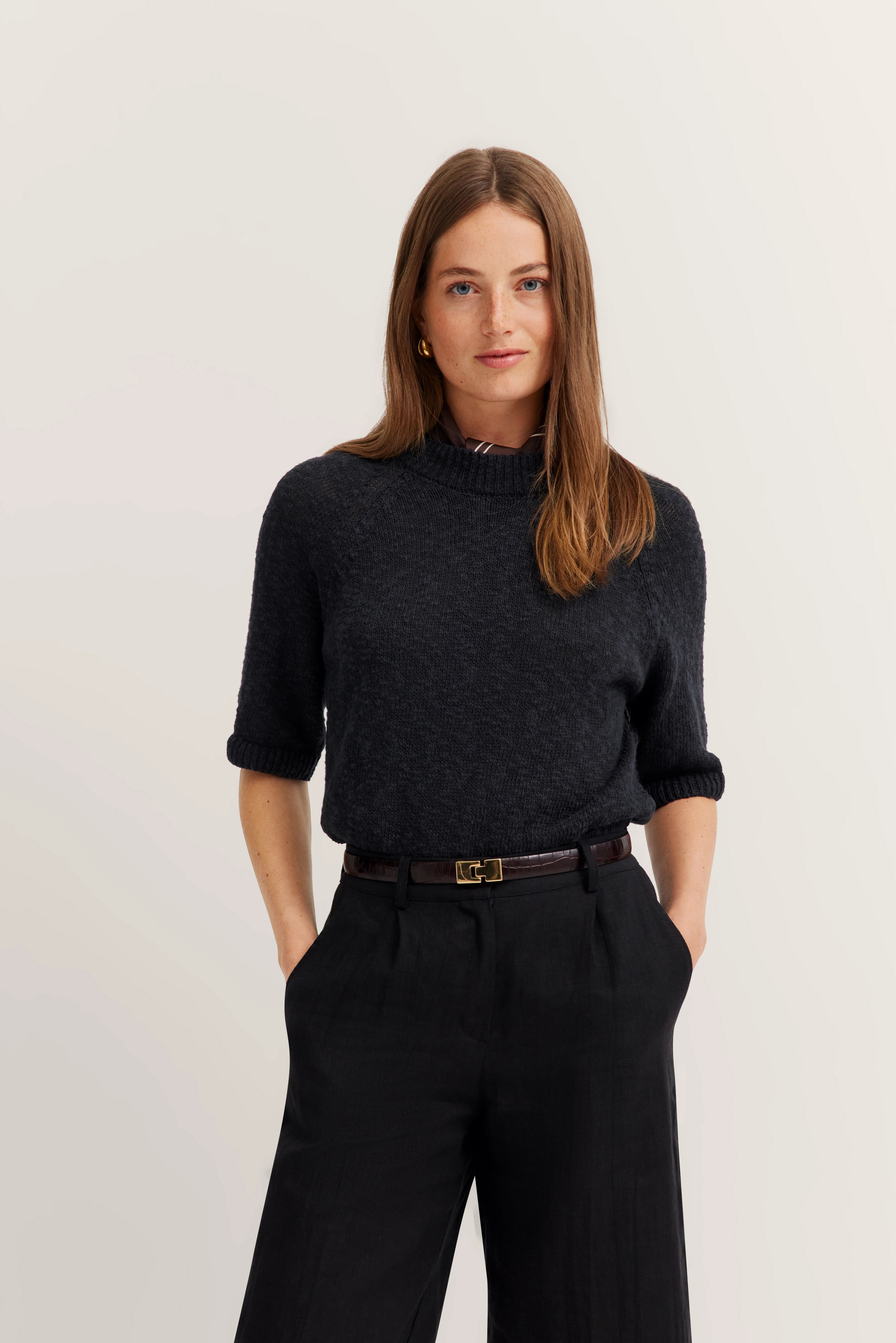 Schwarzer Pullover und Hose, legeres Modelbild, Hände in Hosentaschen.