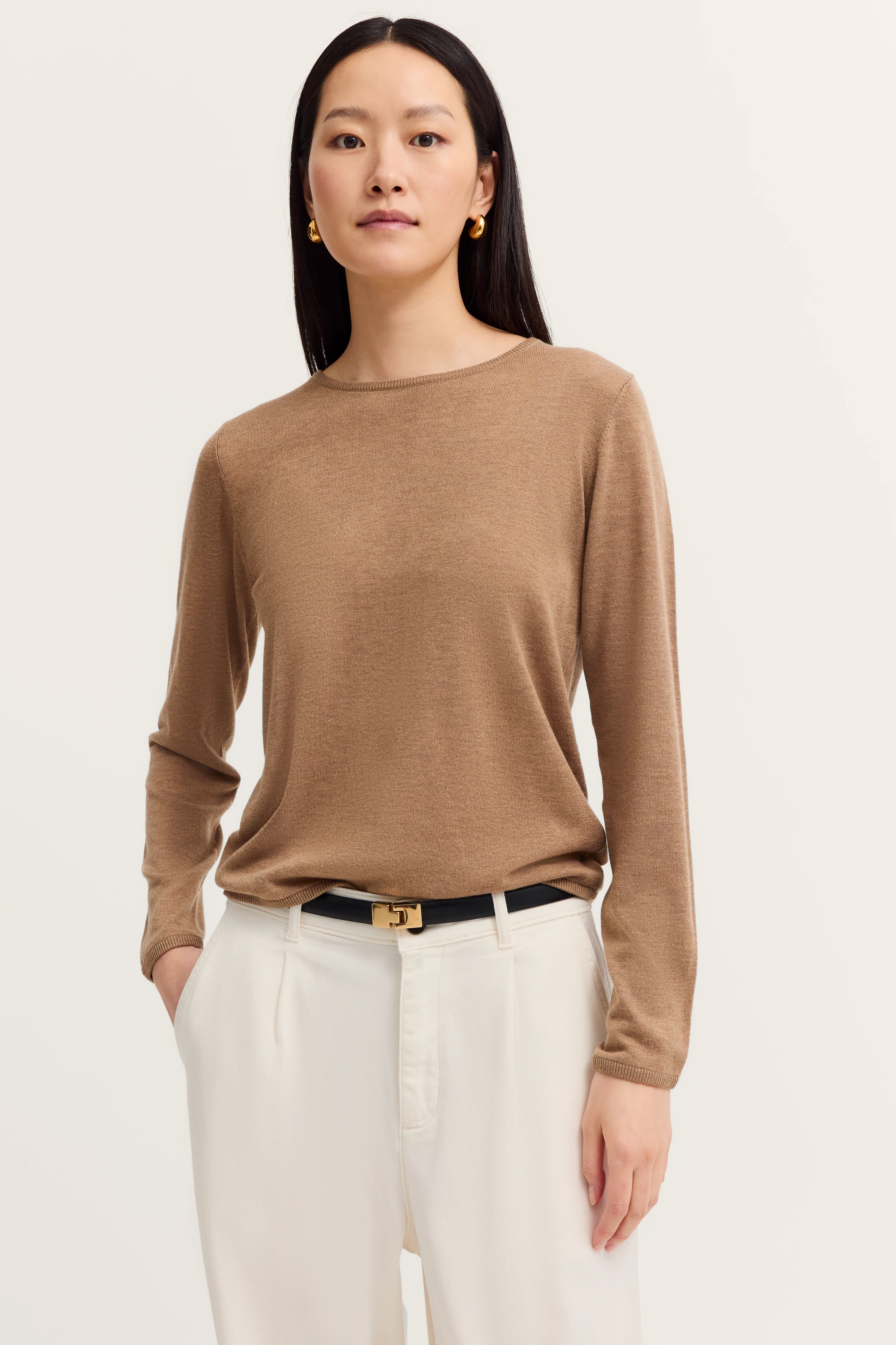 Beige long-sleeve shirt and white pants, model in relaxed pose.