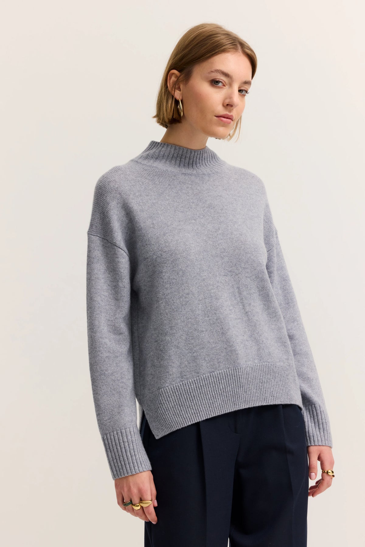 Grauer bugatti Pullover auf Model, legeres Posing, kombiniert mit dunkelblauer Hose.
