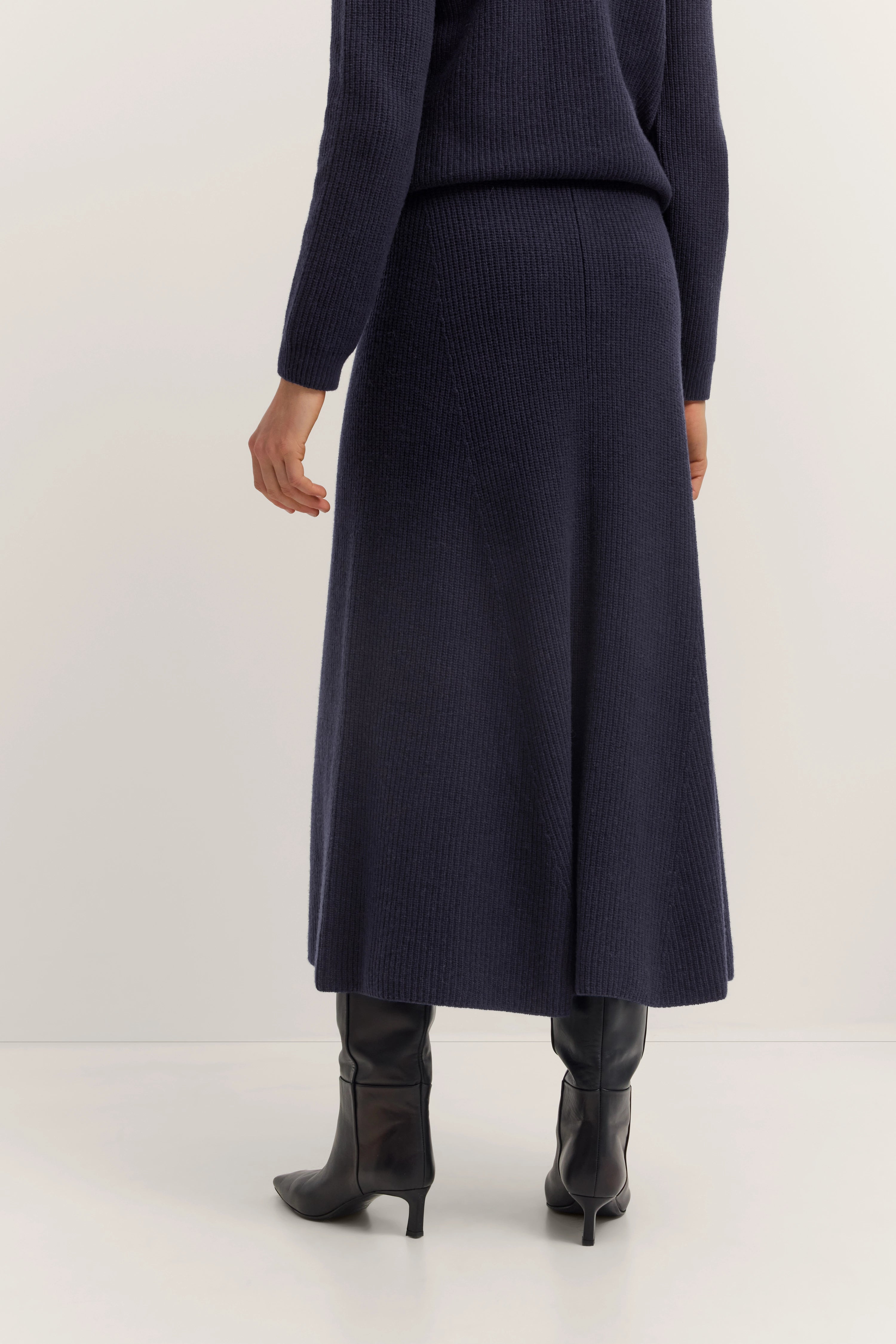 Donkerblauw bugatti breiset met rok en top, model in zijaanzicht, zwarte laarzen.