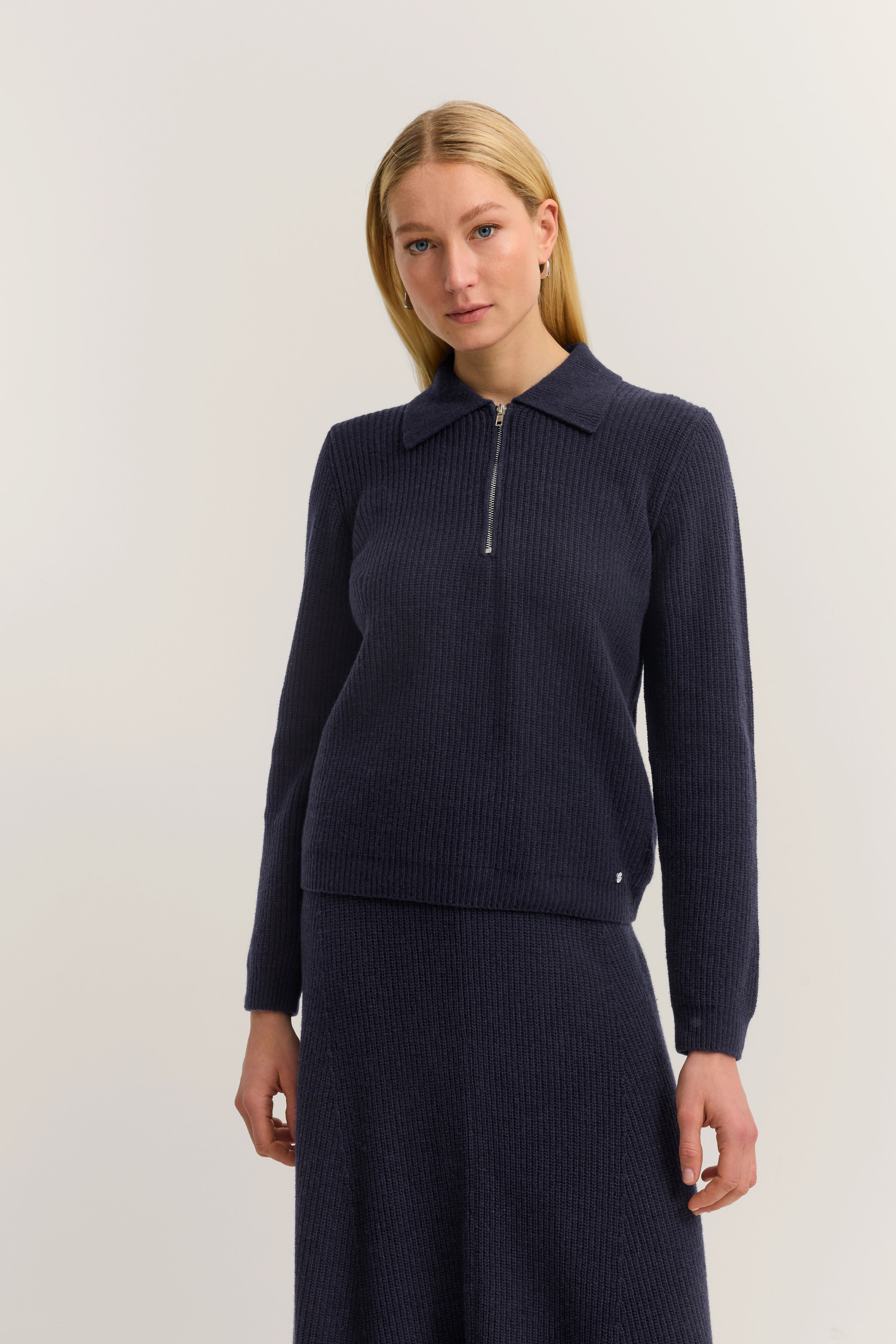 Model in navy Strickpullover mit Reißverschluss und passendem Rock, entspanntes Posing.