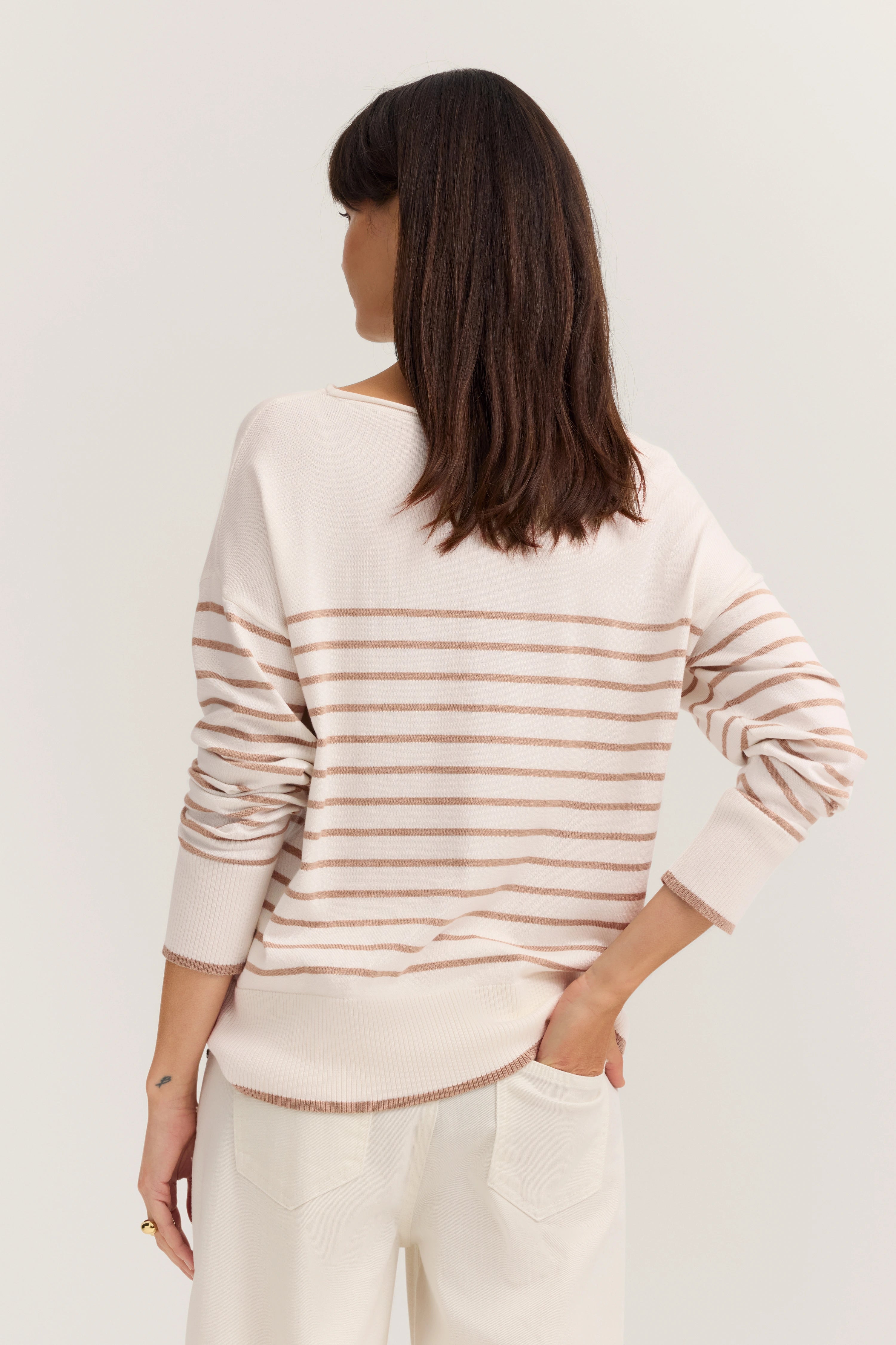 Modelbild im gestreiften Pullover in Beige-Weiß mit legerer Pose von hinten.