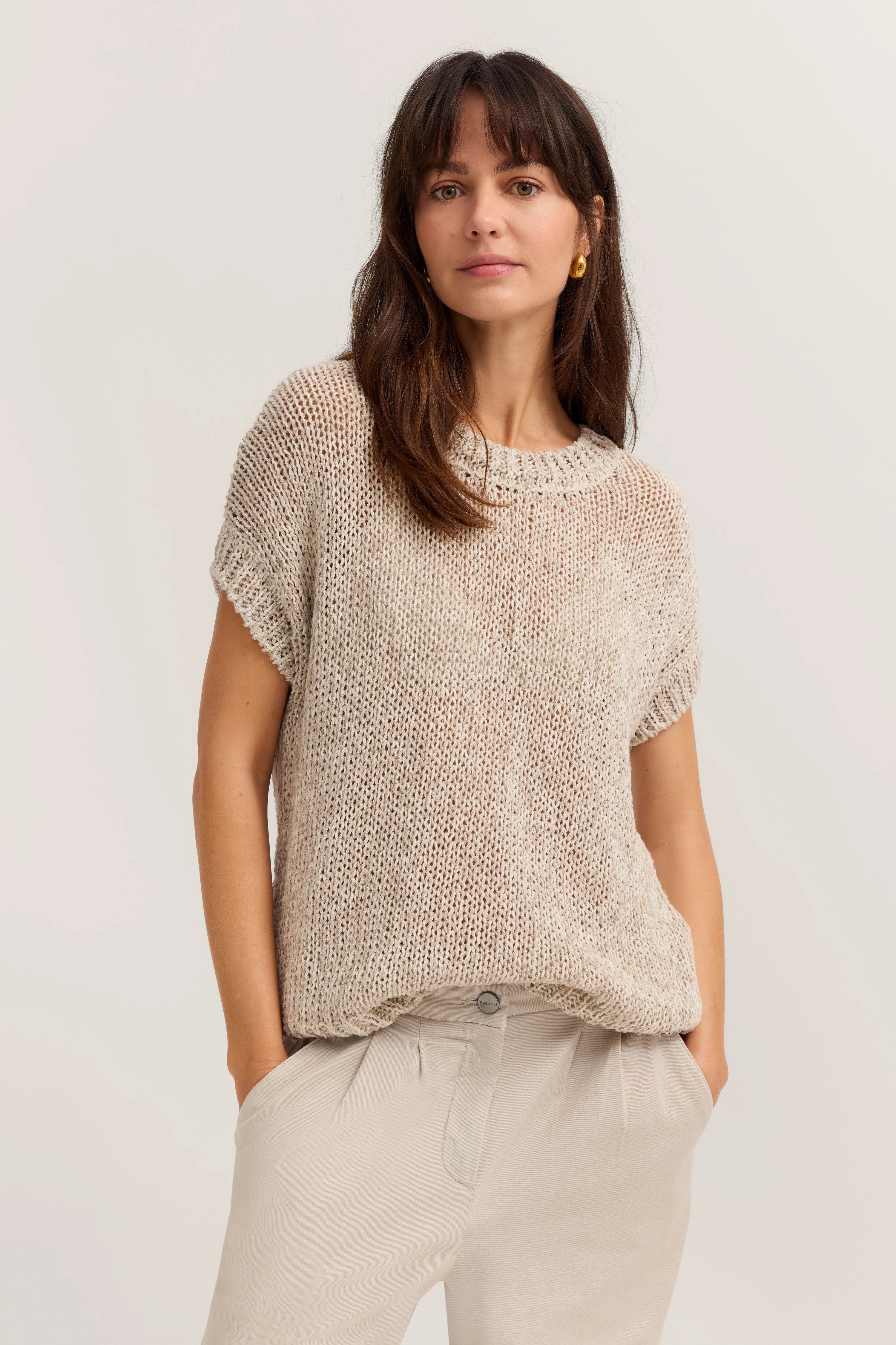 Beiges Stricktop und helle Hose, Modelbild, lässige Pose mit Händen in den Hosentaschen.