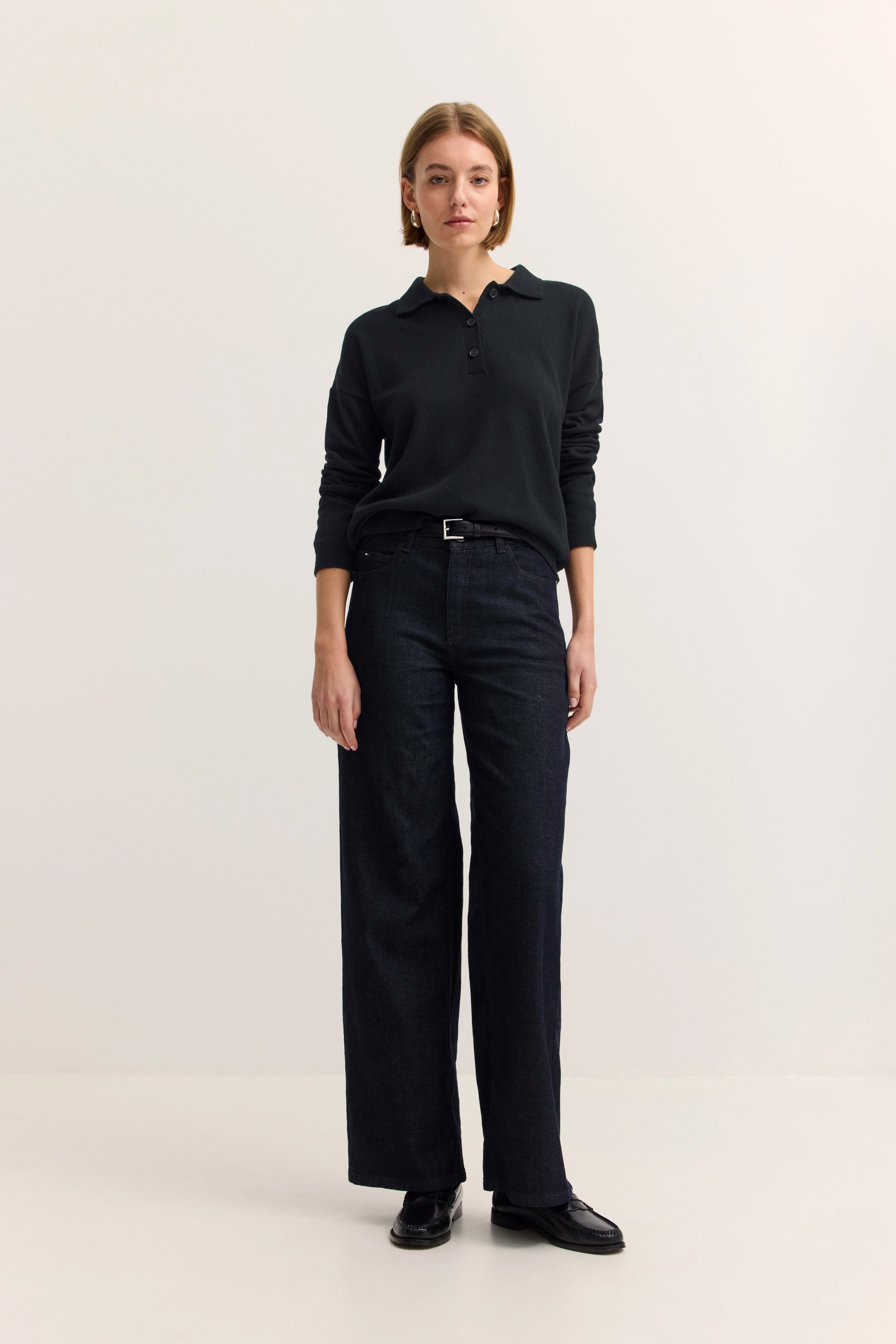 Model in schwarzem Pullover und dunkler Jeans, steht gerade.