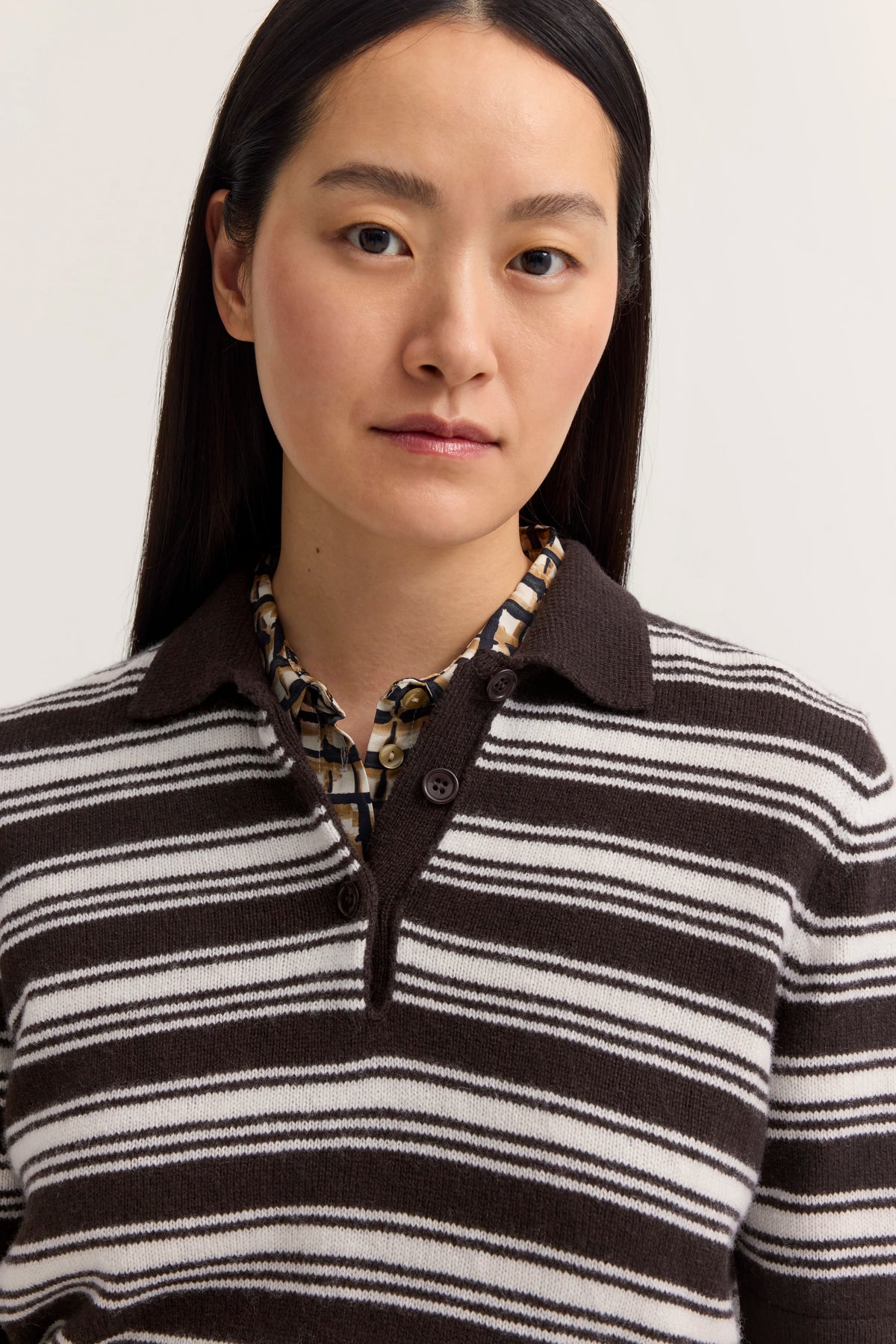 Braun-weiß gestreifter Pullover mit gemusterter Bluse, Model von hinten, lässige Pose.