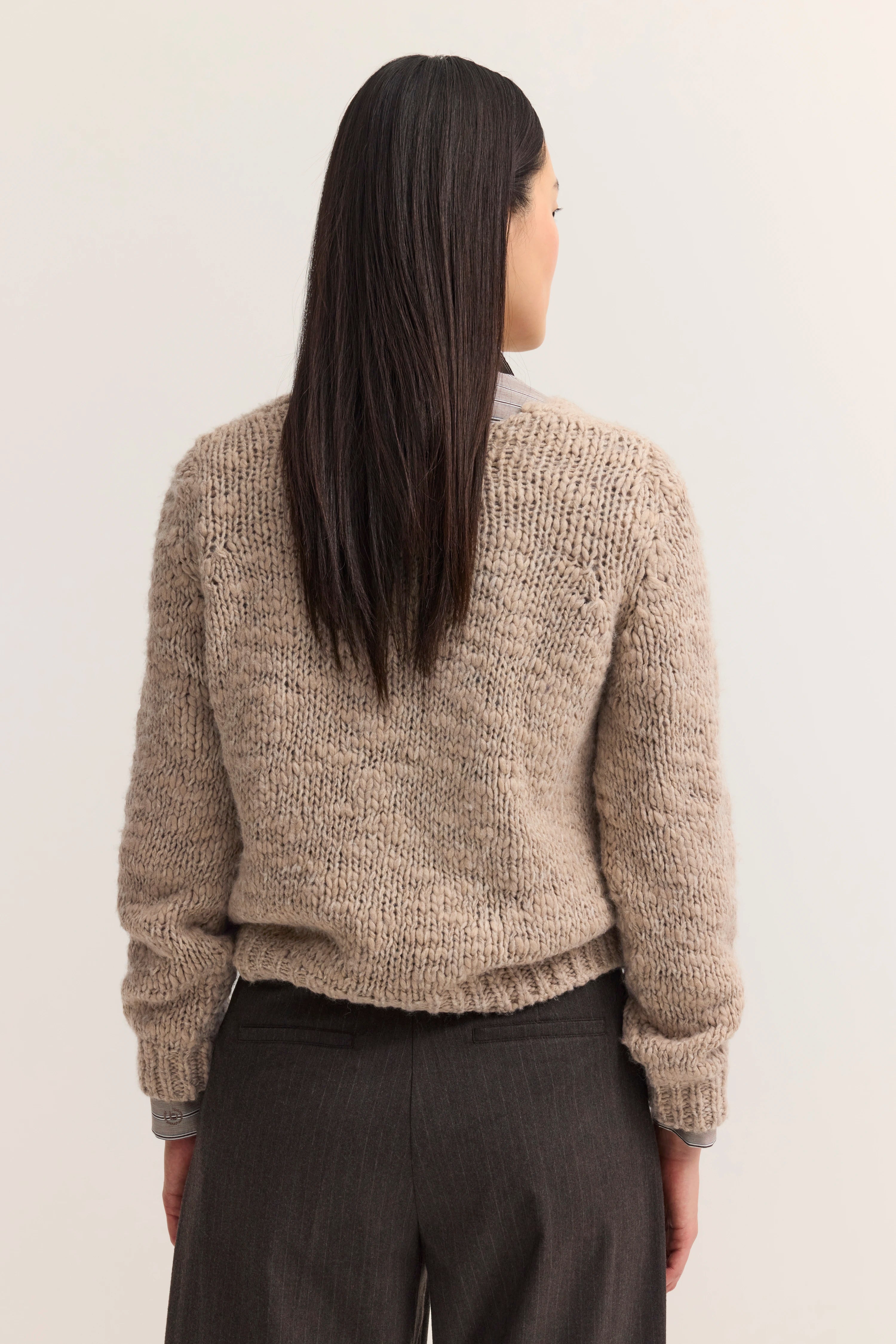 Beiger Strickpullover und graue Hose, Model von hinten, legeres Posing.