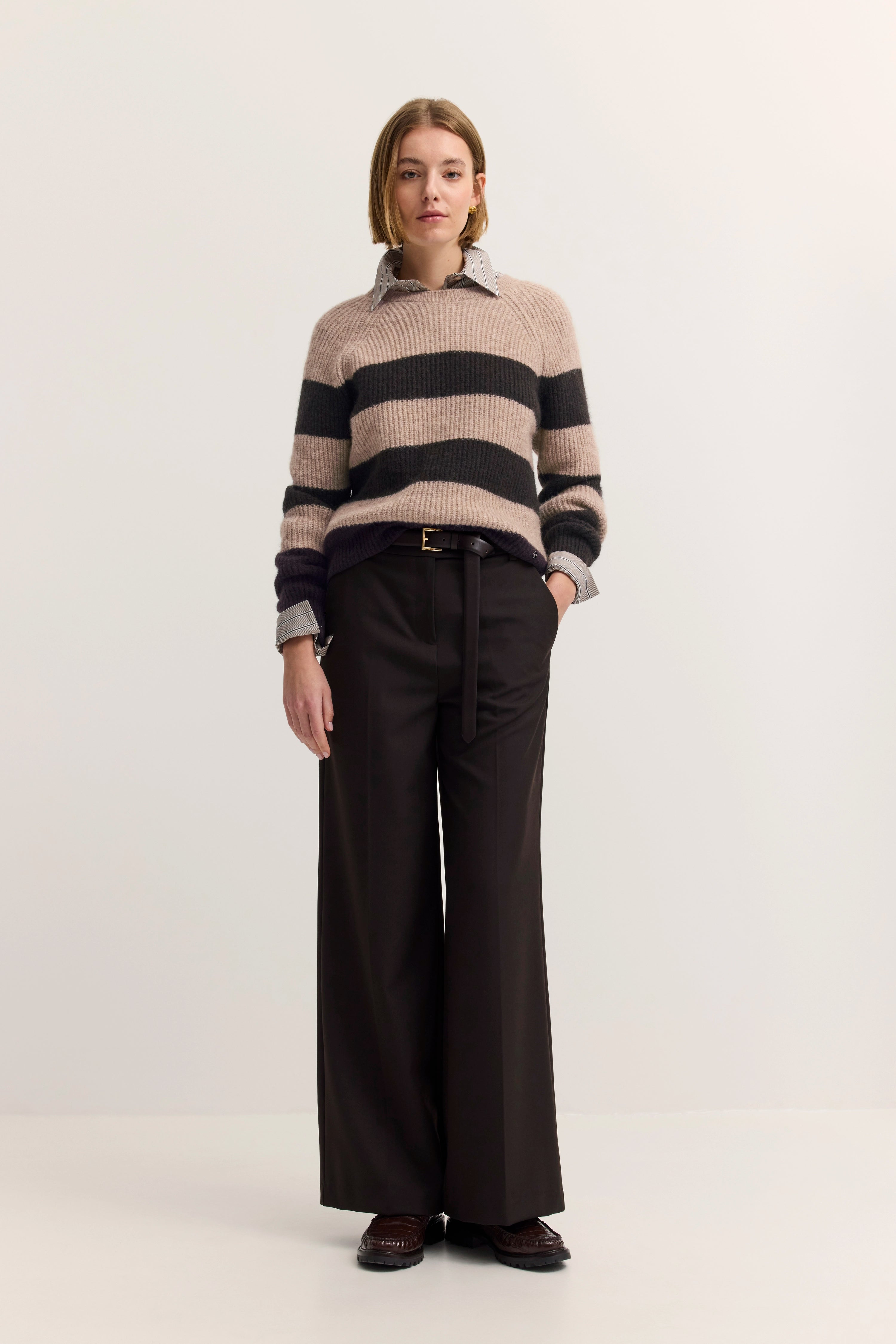 Model in gestreiftem Pullover und schwarzer Hose, entspannte Pose, bugatti Stil.