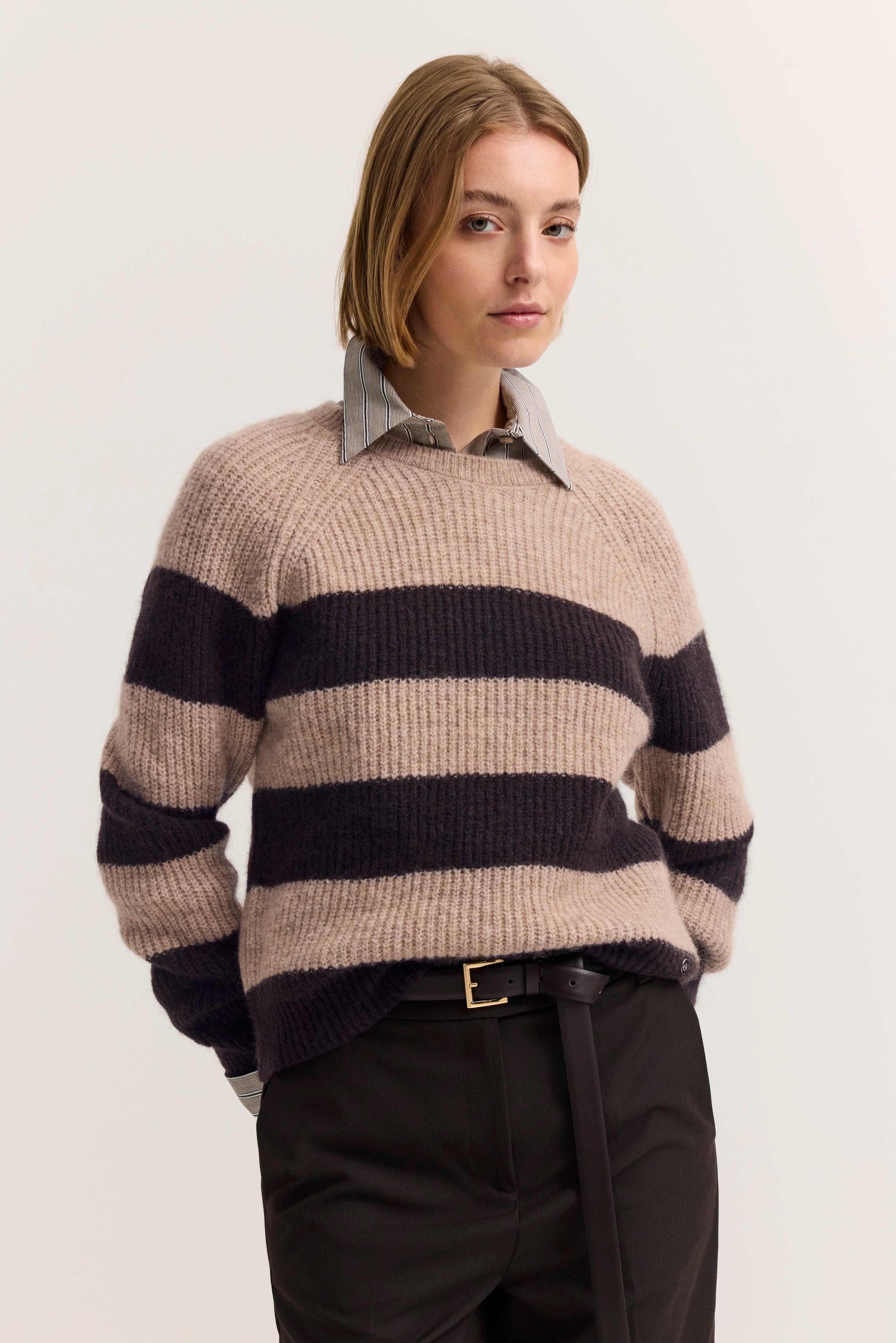 Alt-Text: Modelbild, beige-schwarzer Streifenpullover, schwarzes Hemd, lässige Pose, bugatti Stil.
