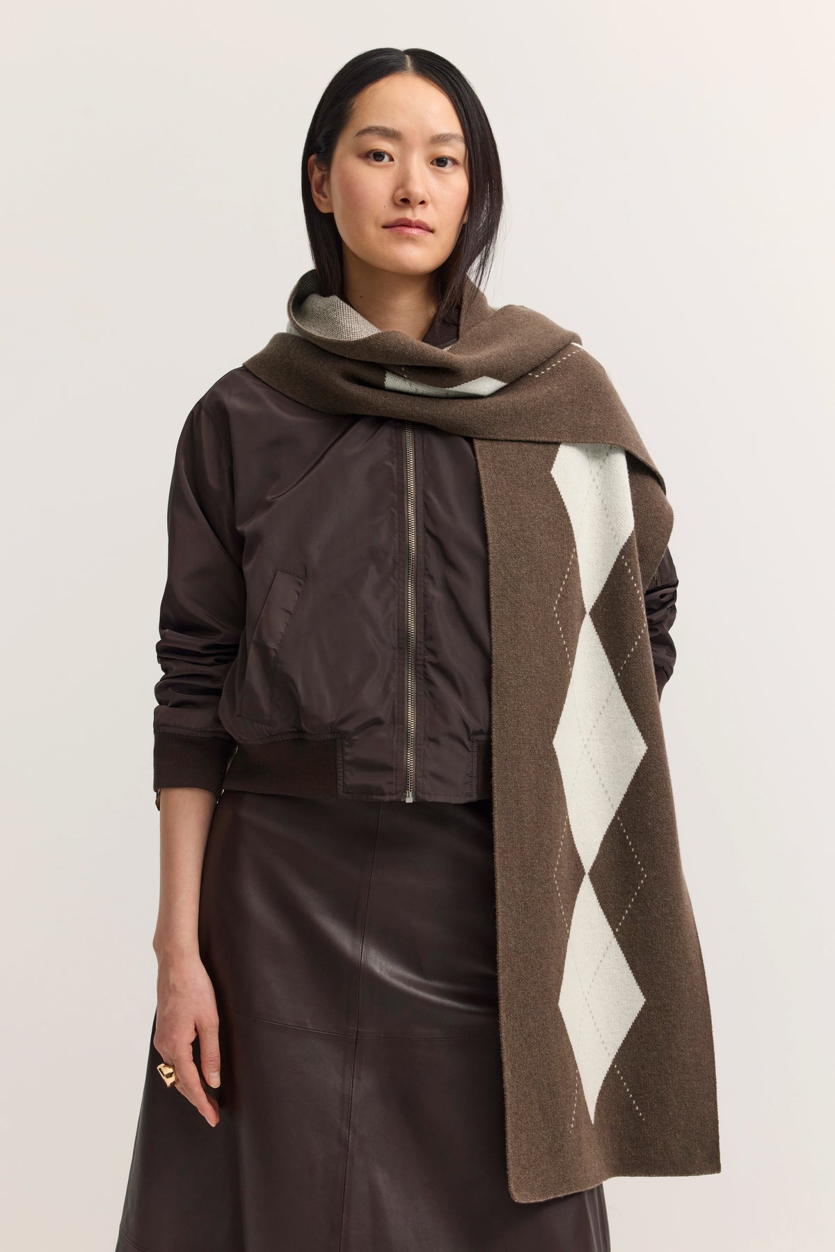 Braune Jacke mit braunem Lederrock, Model mit braunem Schal, argyle Muster, lässige Pose.