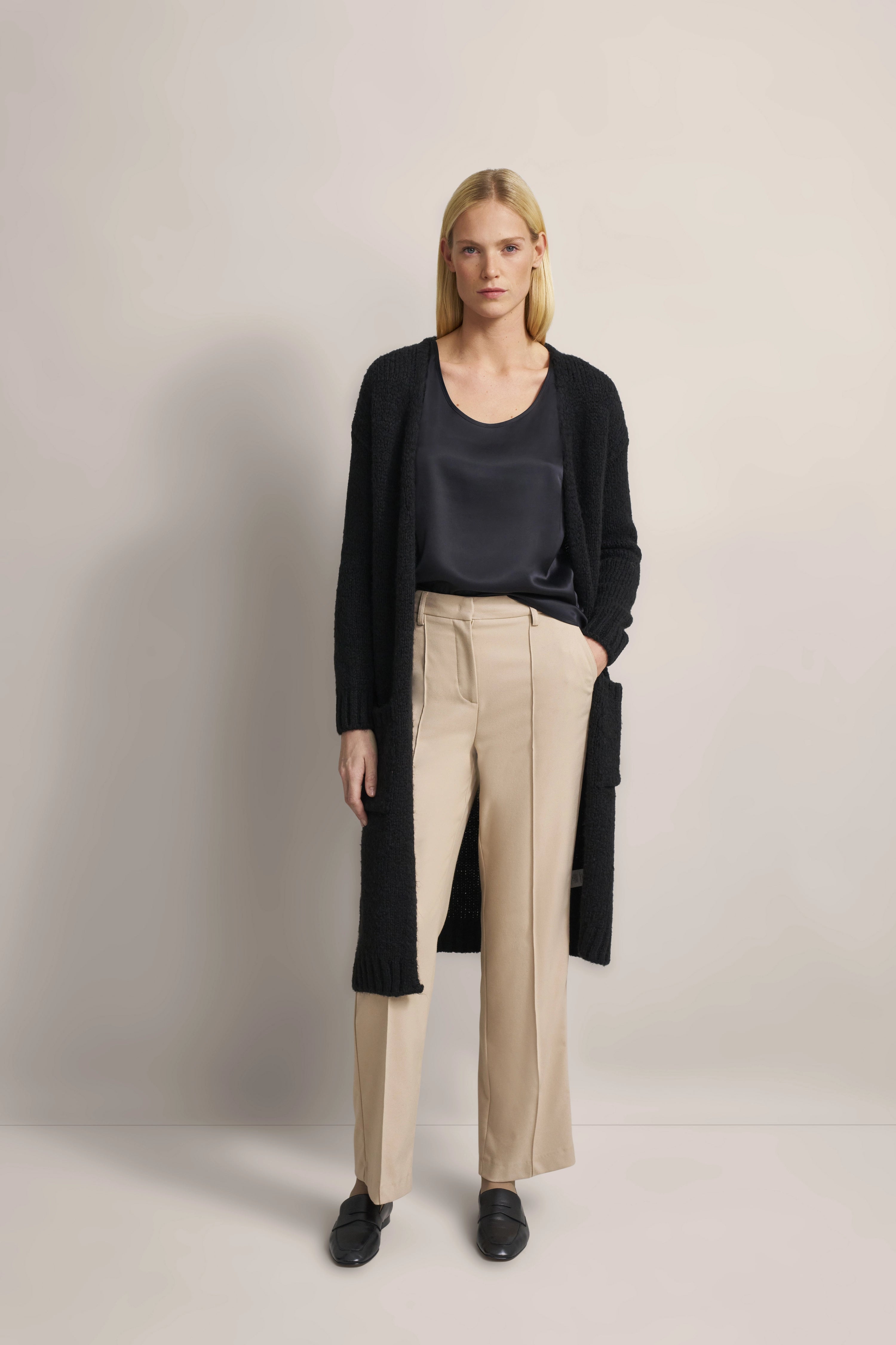 Model in schwarzem Cardigan, dunklem Top und beigen Hosen von bugatti, entspannte Haltung.