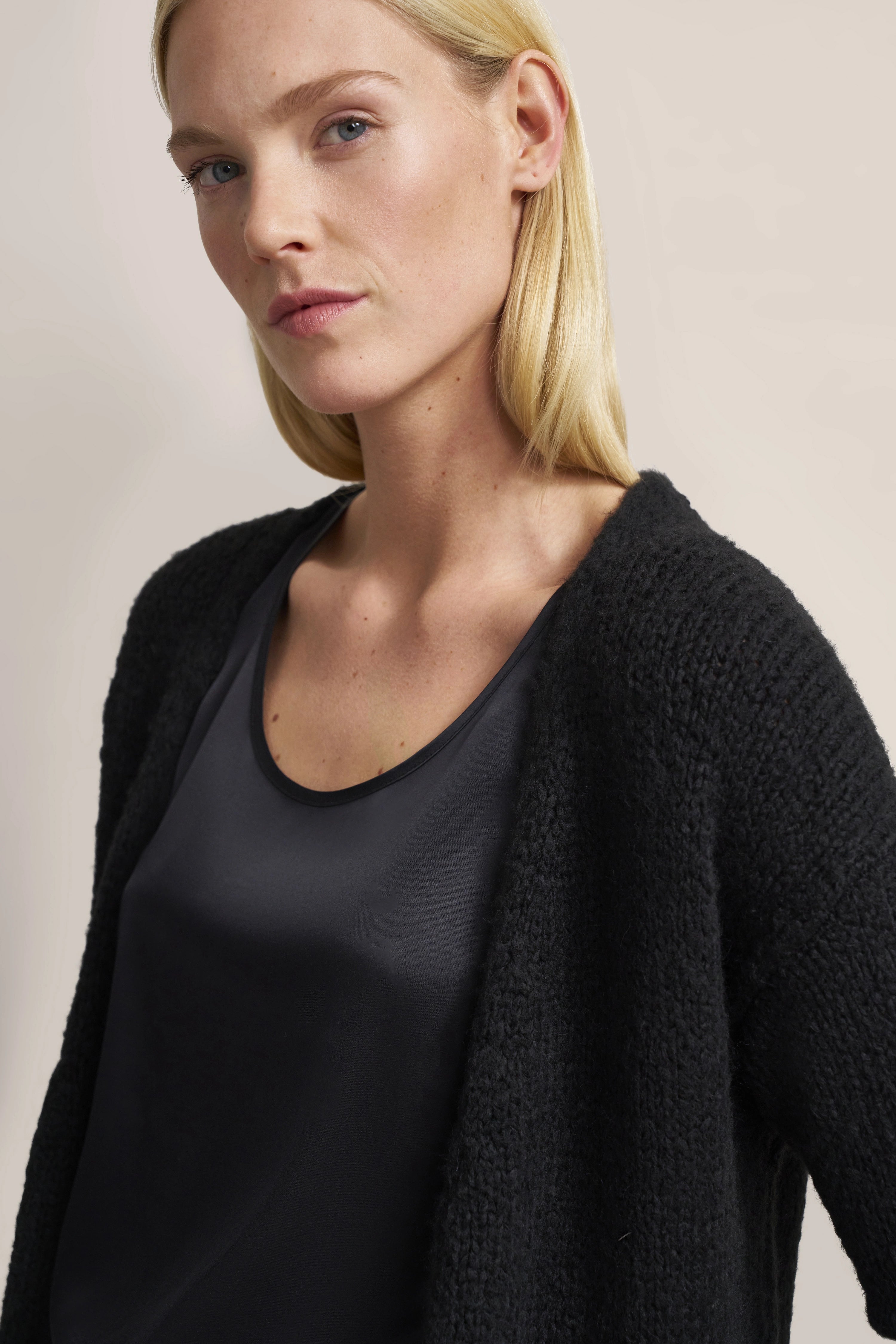 Büstenbild mit schwarzem bugatti Top und Strickjacke, lässiger Look, minimalistisches Design.