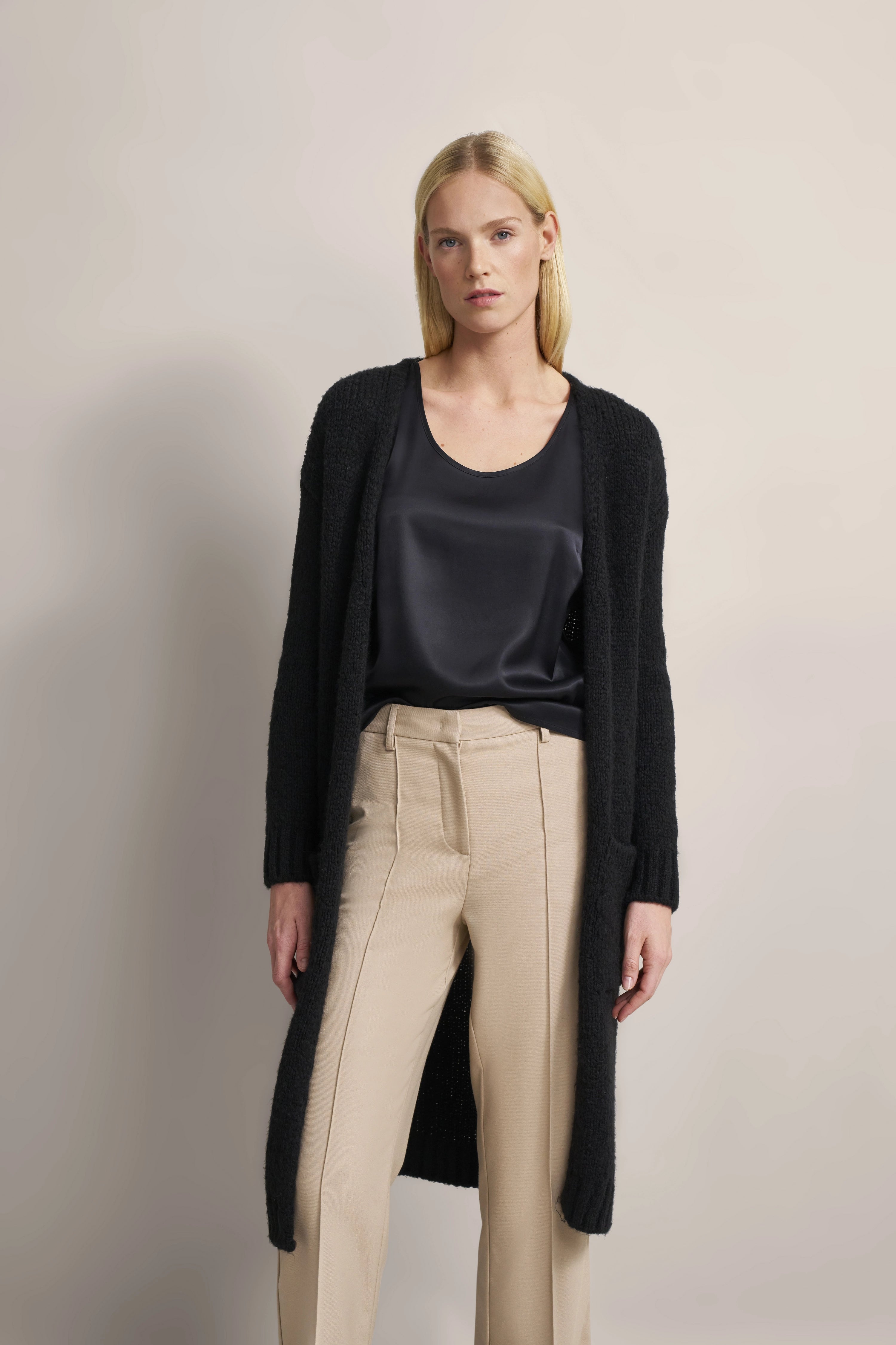 Model trägt schwarzen bugatti Cardigan, dunkles Top und beige Hose, entspanntes Posing.