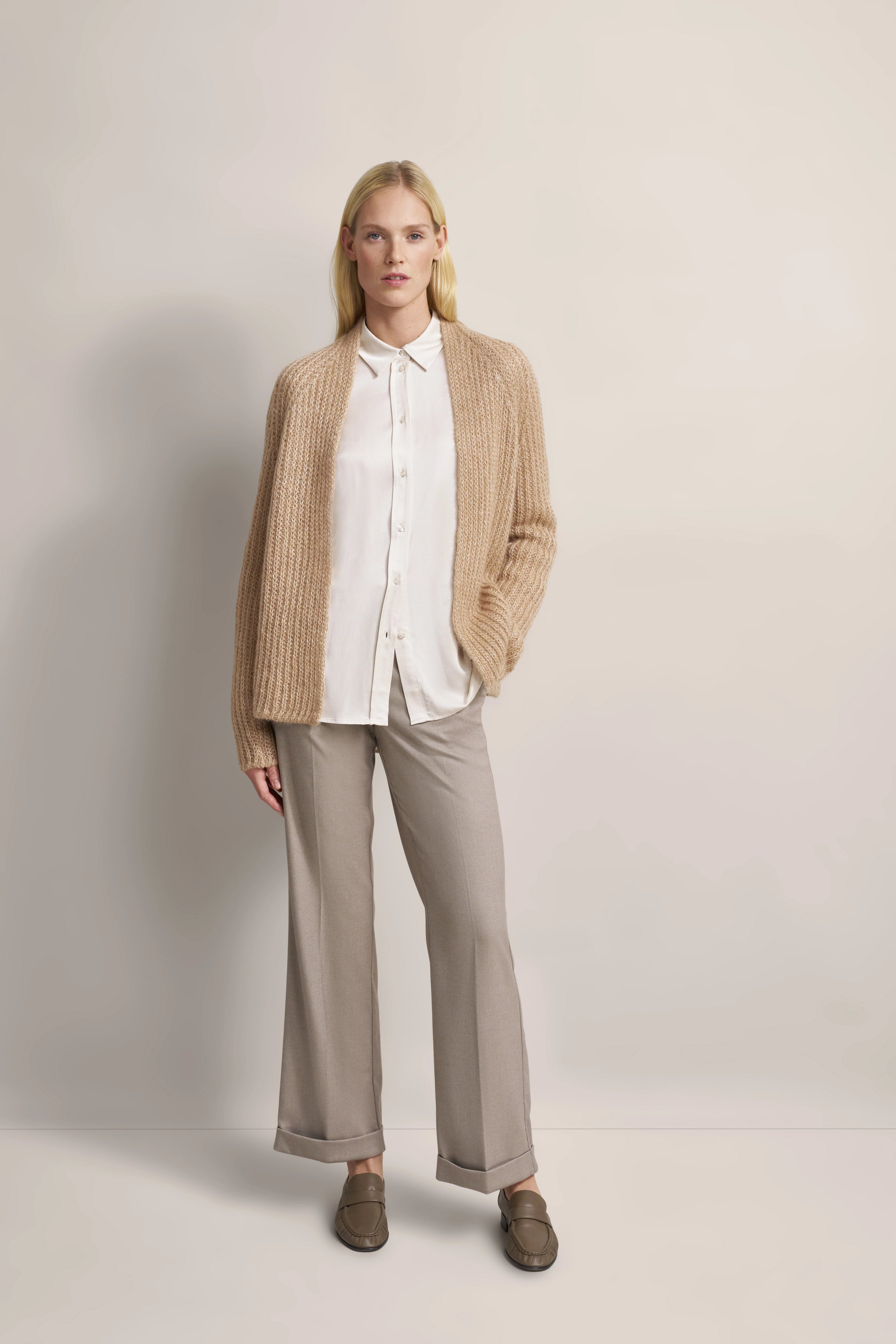 Model in beigem Cardigan, weißer Bluse, grauer Hose, legeres Posing.