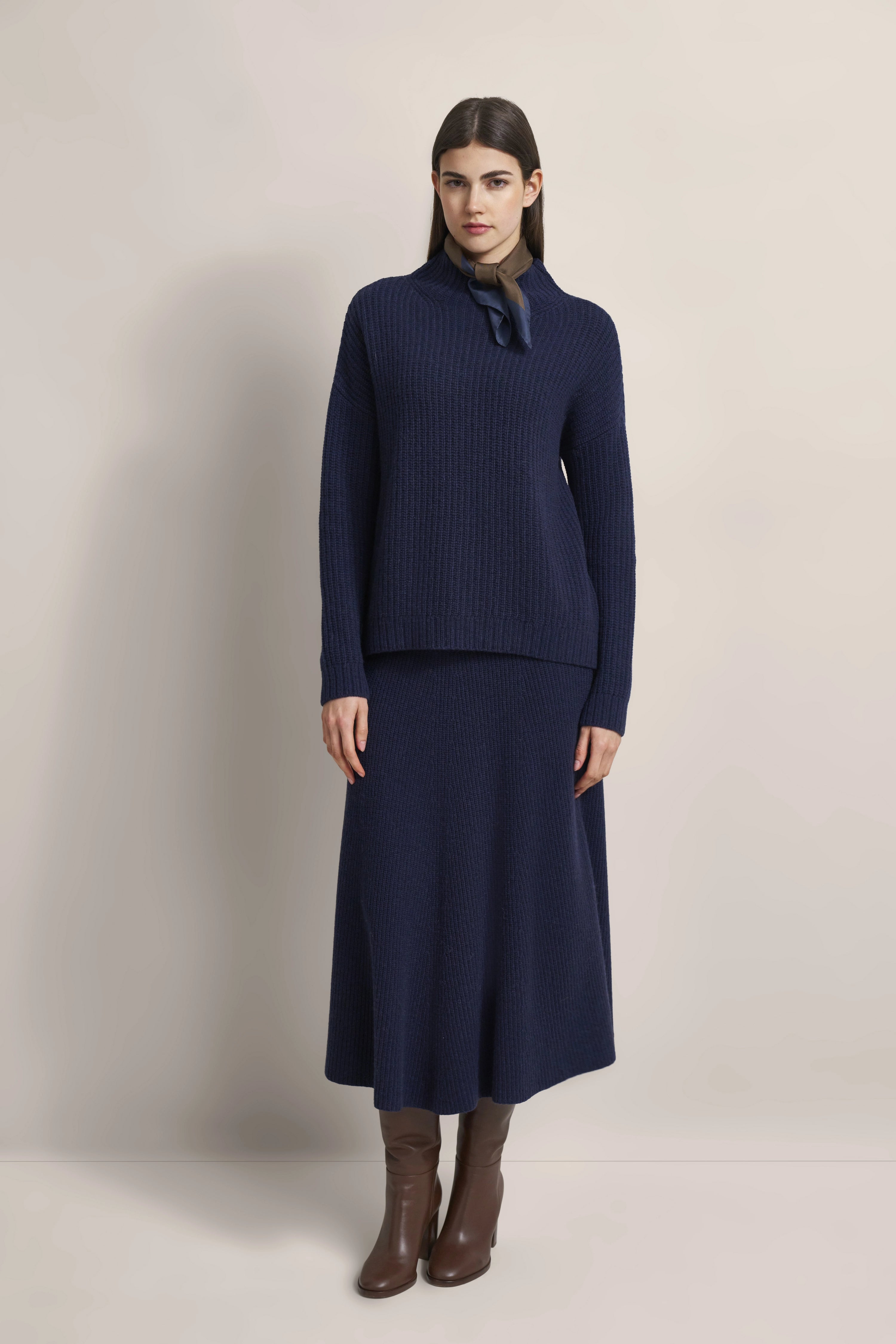 Model in navy knit dress and brown boots standing. Outfit by bugatti.