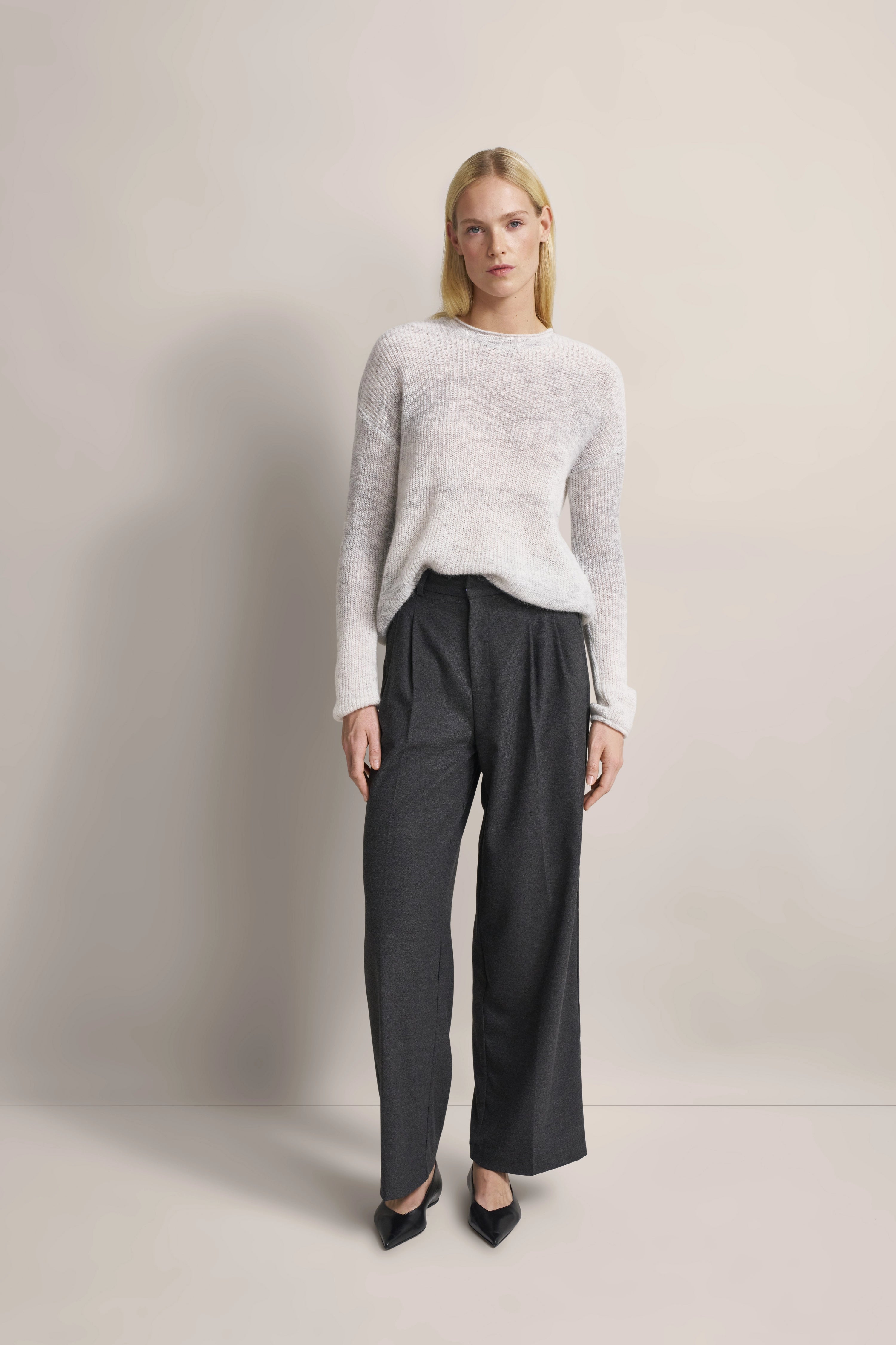 Model trägt grauen Strickpullover und dunkelgraue Hose, entspannte Pose.