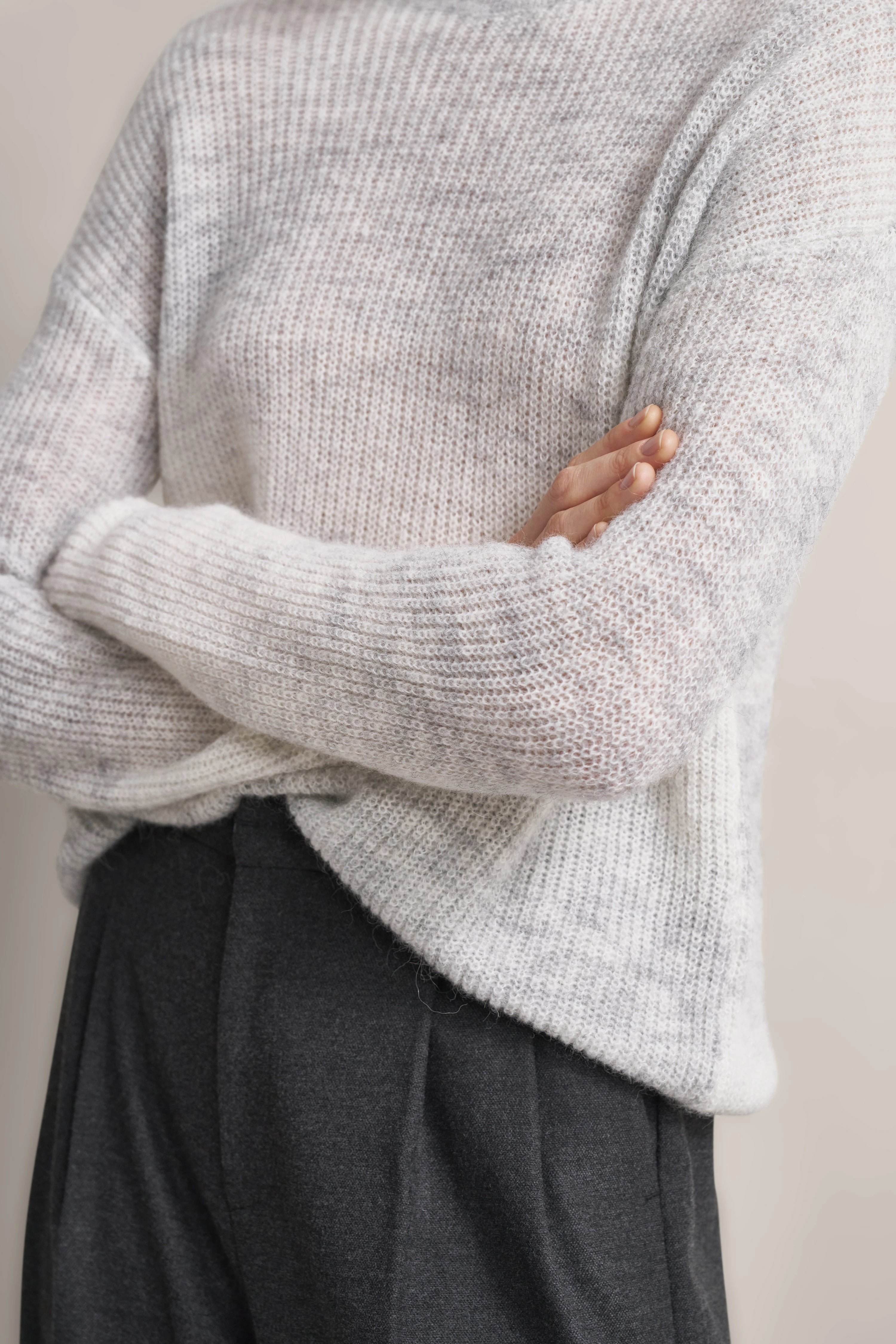 Grauer Strickpullover und dunkelgraue Hose, legeres Büstenbild, Arme verschränkt.