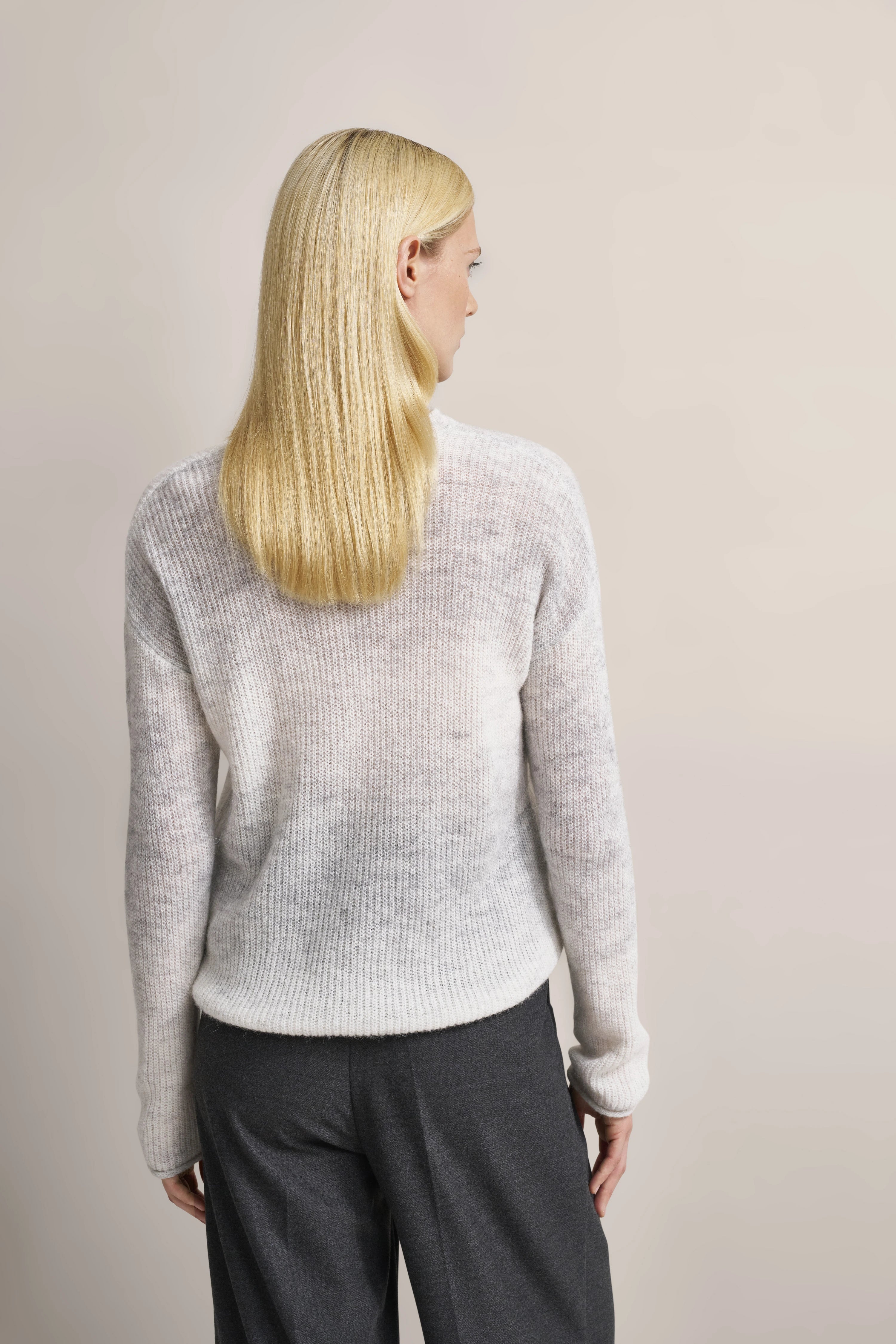 Weißer Pullover und graue Hose von bugatti, Modelbild von hinten, entspanntes Posing.