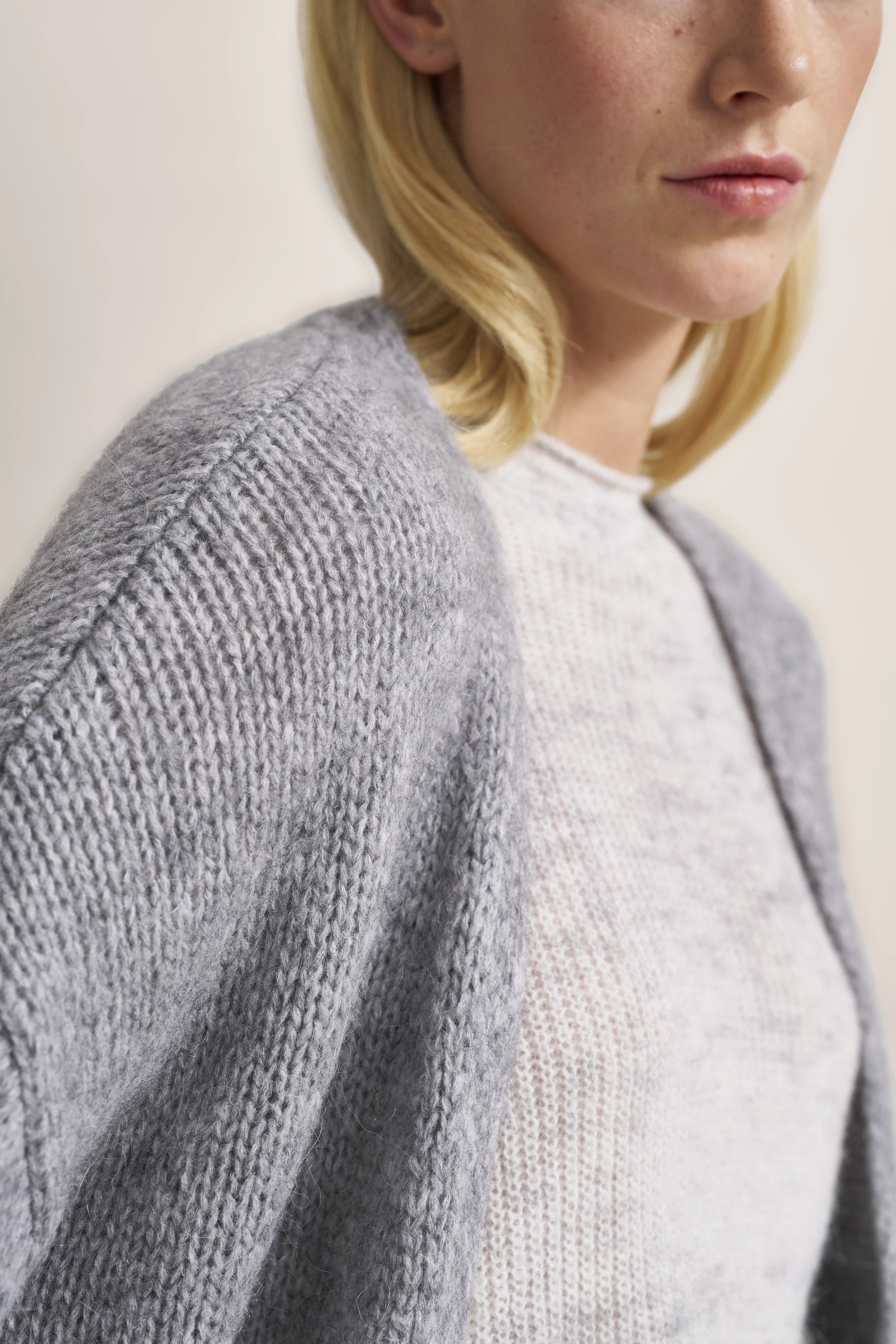 Grauer Strickcardigan über weißem Pullover, Büstenbild, entspanntes Styling.