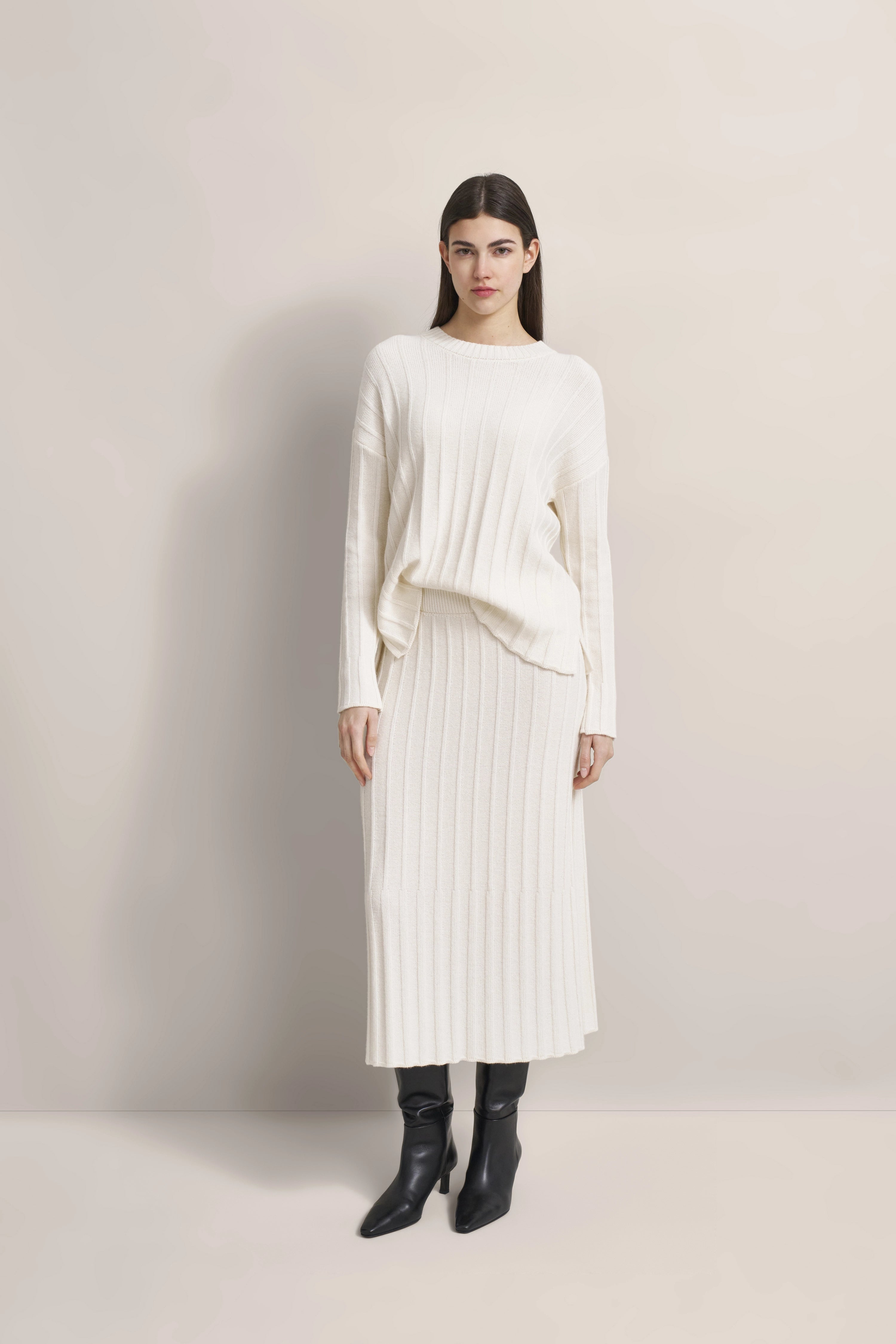 Weißer Strickpullover und Rock, Modelbild, entspannte Pose, schwarze Stiefel, bugatti Stil.