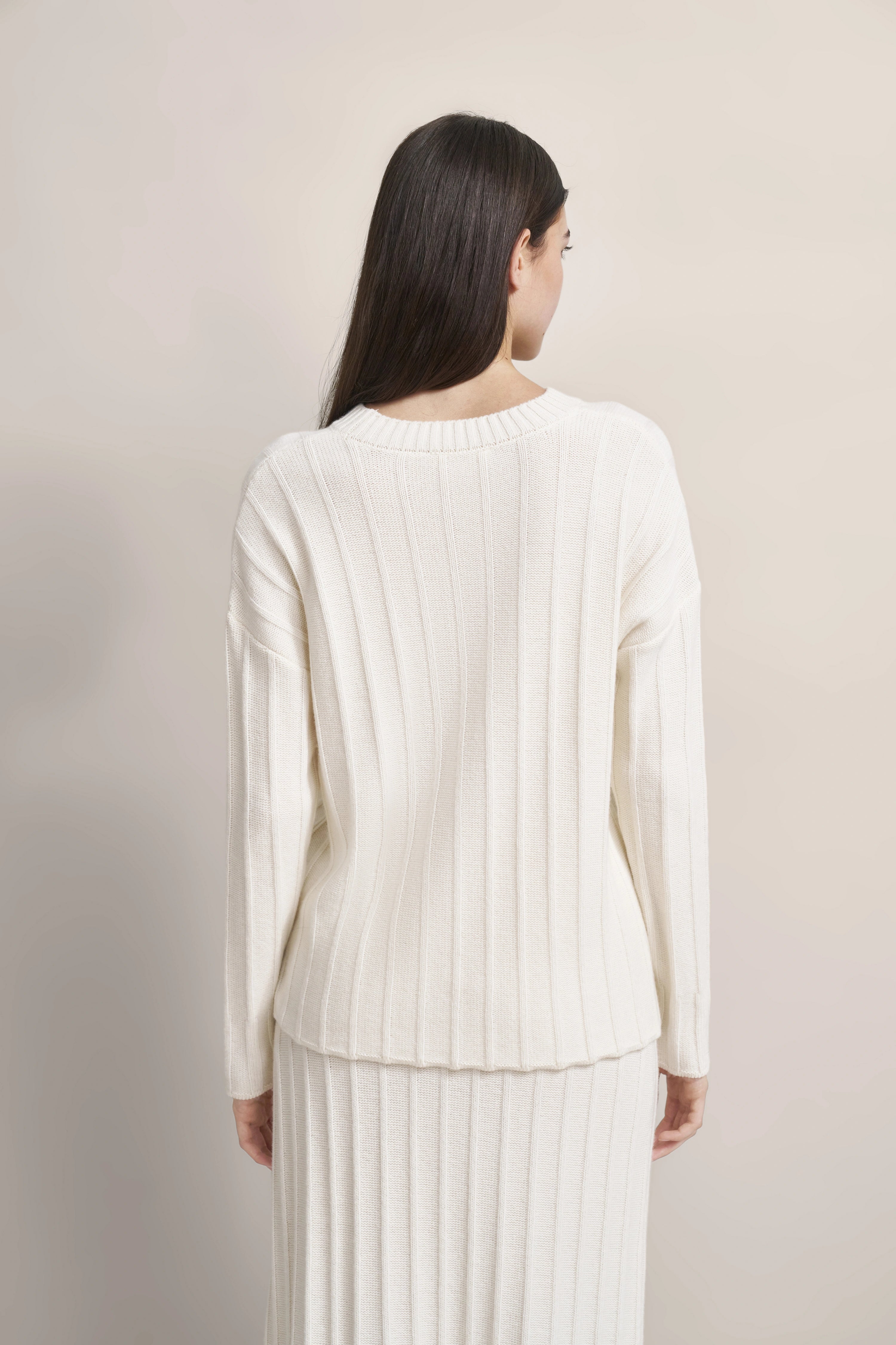 Rückenansicht Model in weißem, geripptem bugatti Pullover und Rock, legeres Posing.