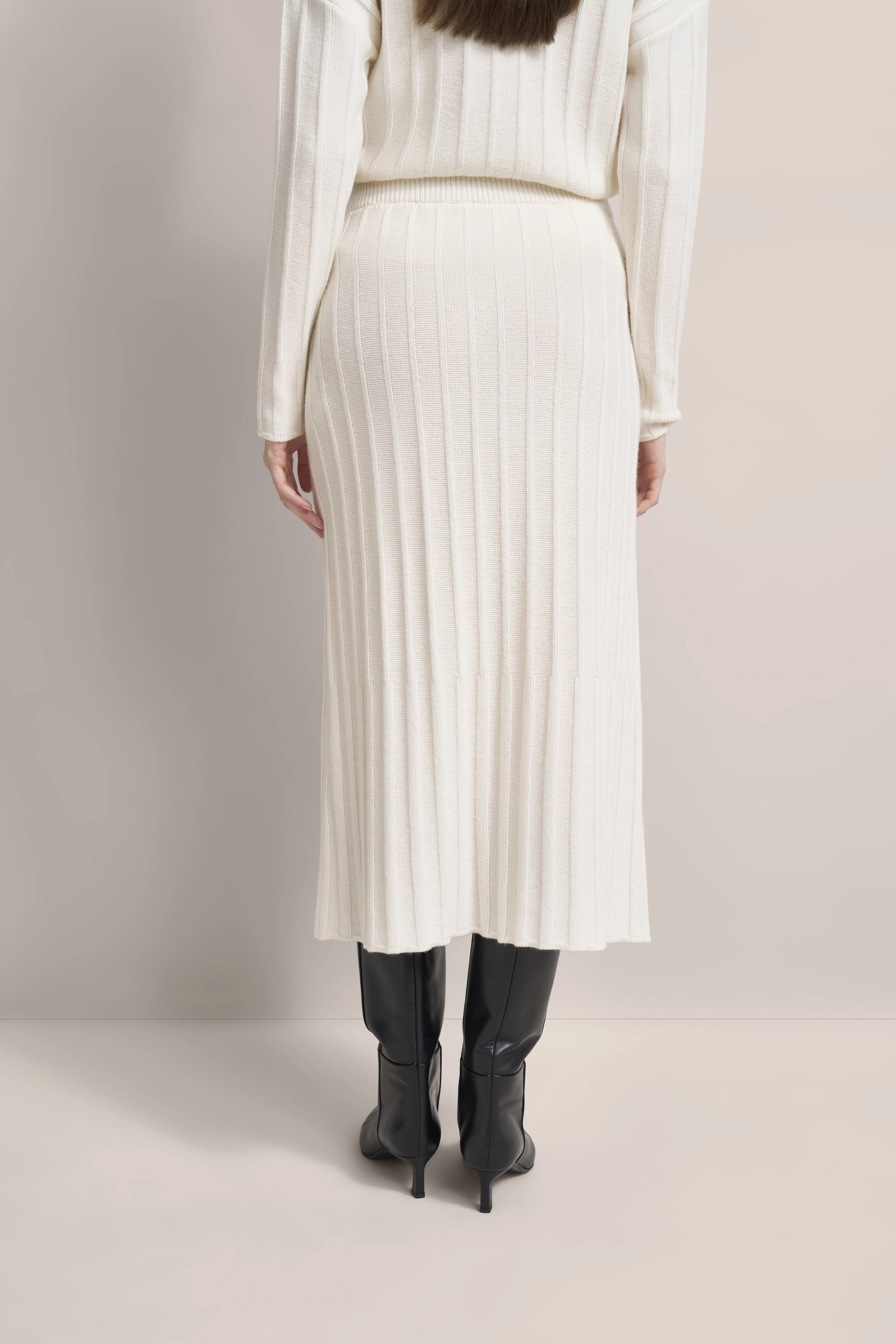 Weißes geripptes Strickkleid, schwarzer Stiefel, Modelbild, Rückenansicht, schlichtes Posing.