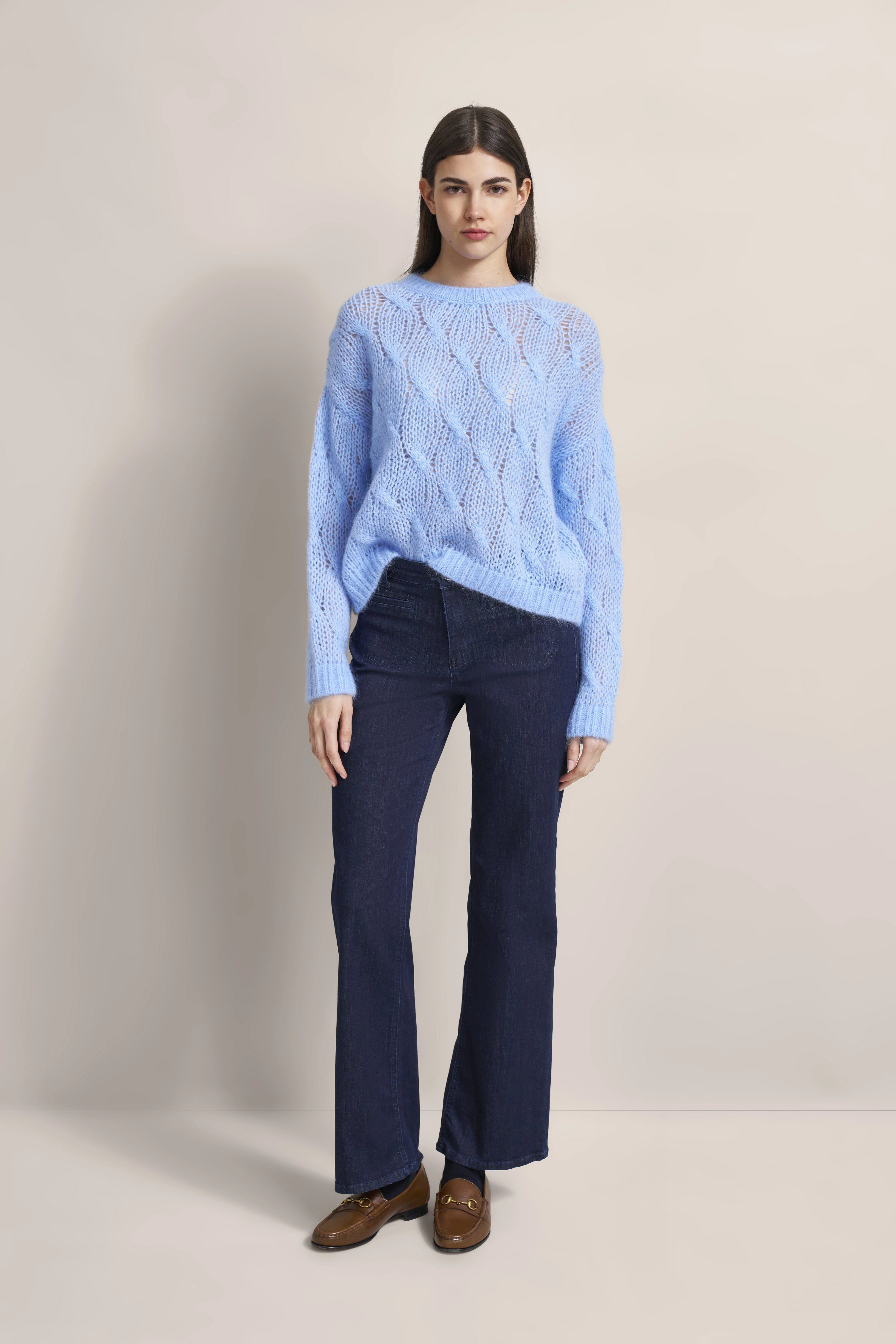 Blauer Strickpullover mit Zopfmuster, dunkelblaue Jeans, braune Loafer. Model posiert stehend.