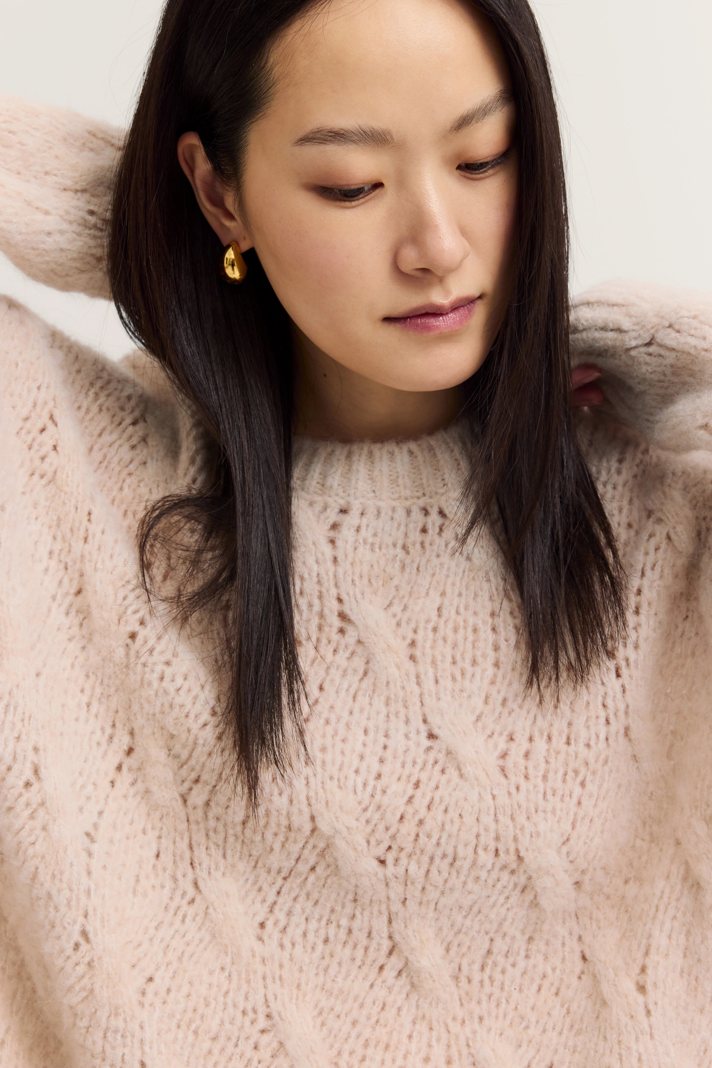 Woman in beige knit sweater, casual pose, hands in hair, elegant style by bugatti.
