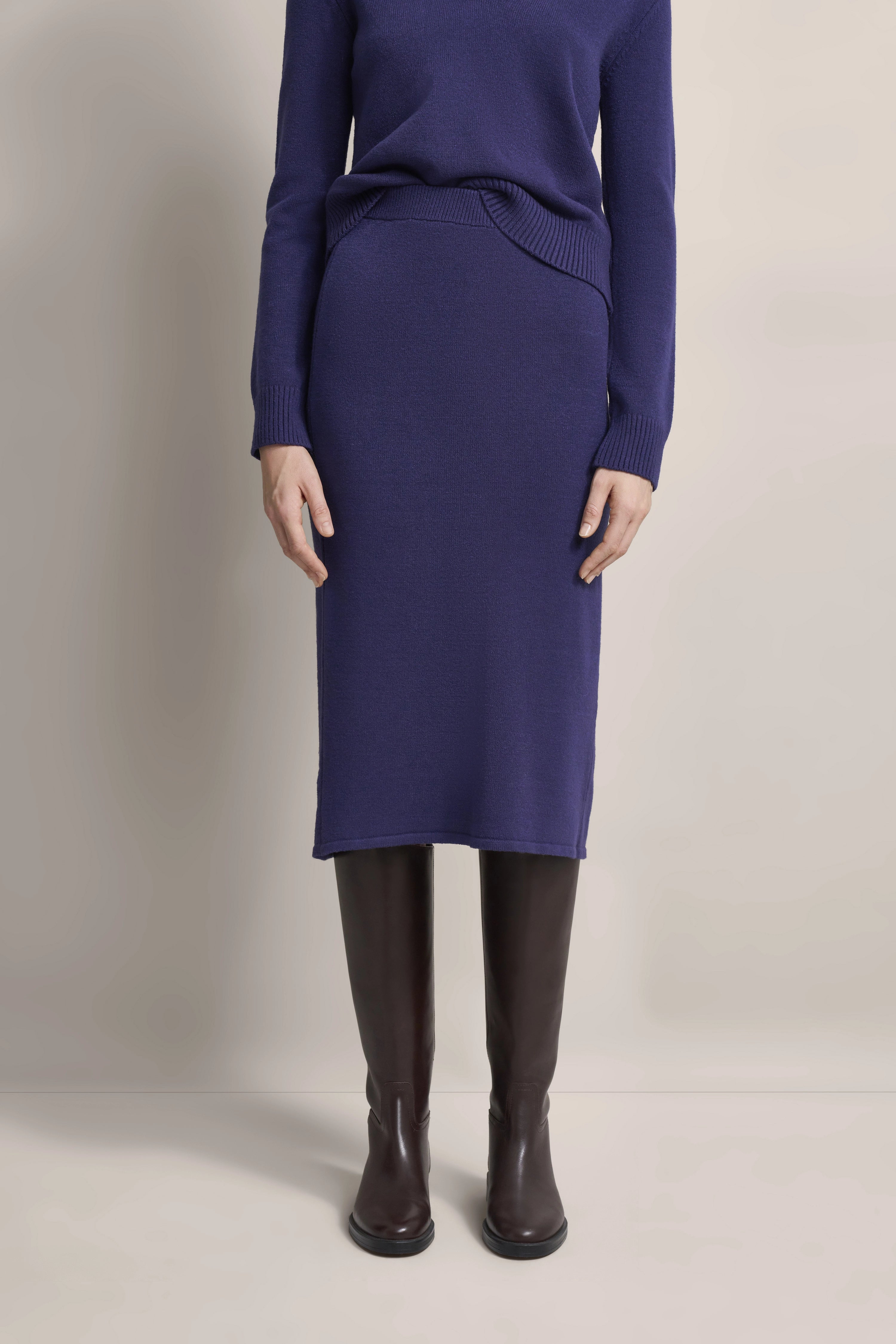 Lila bugatti Strickset mit Rock und Pullover, Modelbild, lässig stehend mit braunen Stiefeln.