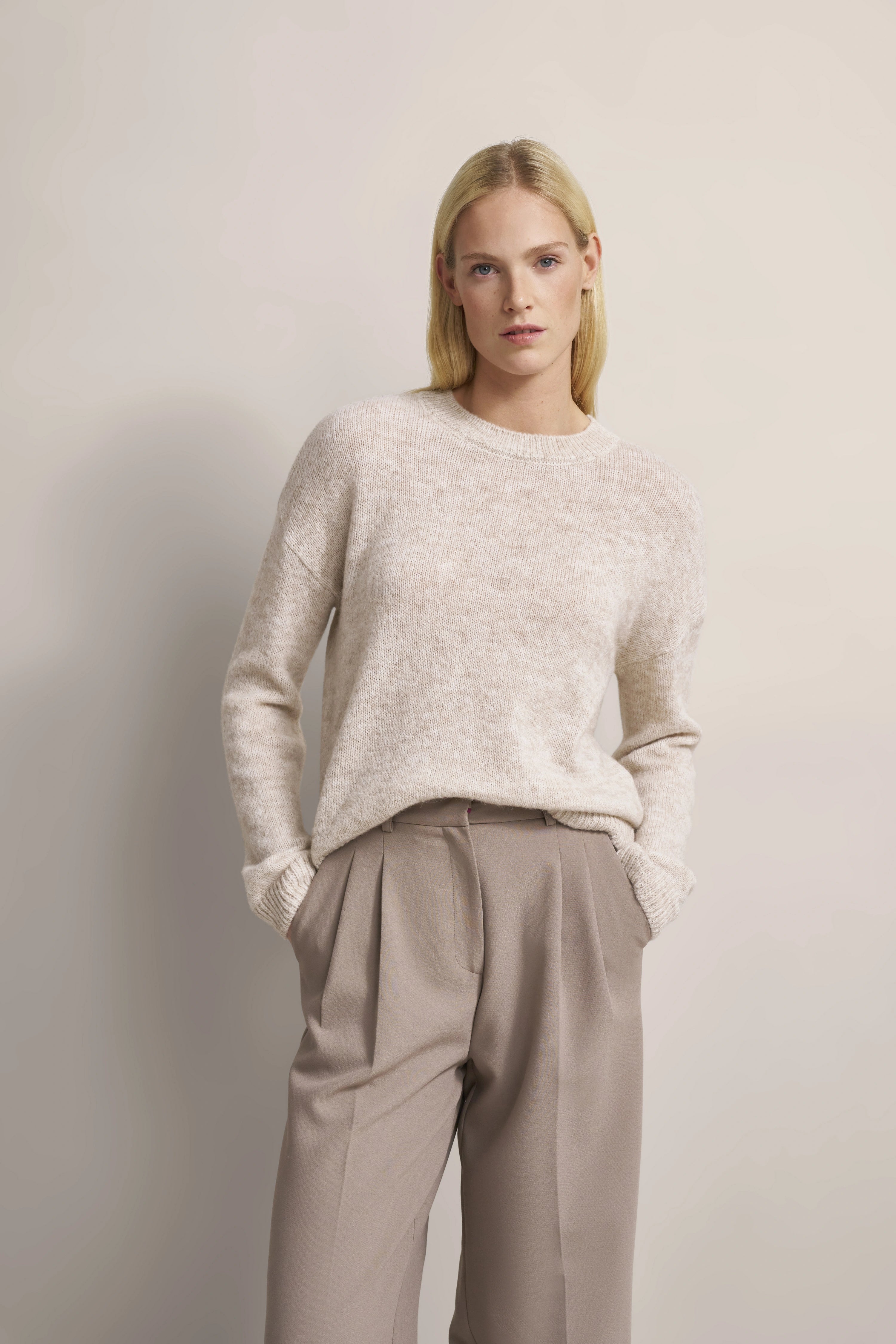 Beiges Outfit: Strickpullover und weite Hose. Model mit Händen in den Taschen.