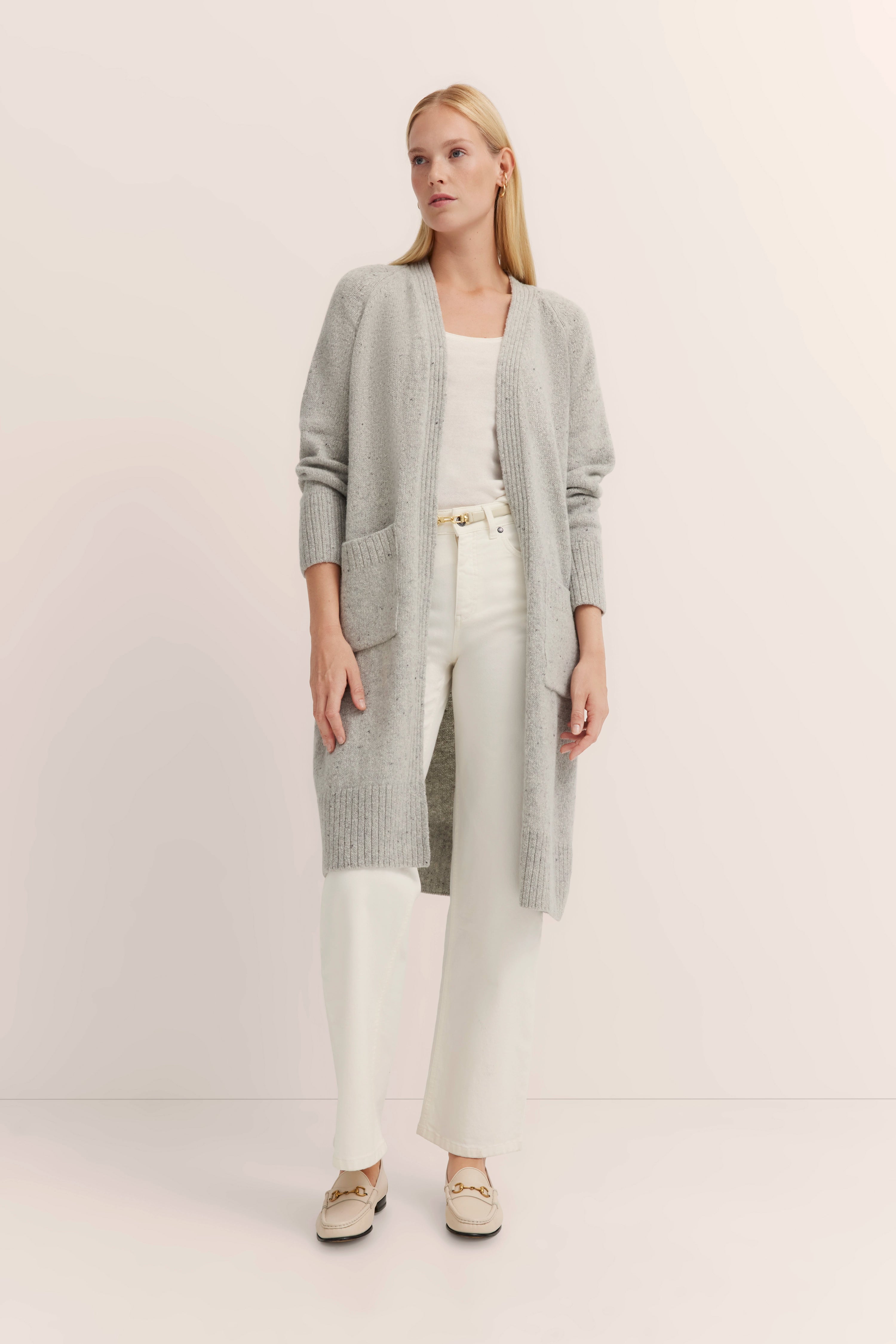 Grauer bugatti Cardigan, weißes Top, weiße Hose, beiges Model, entspannte Pose.