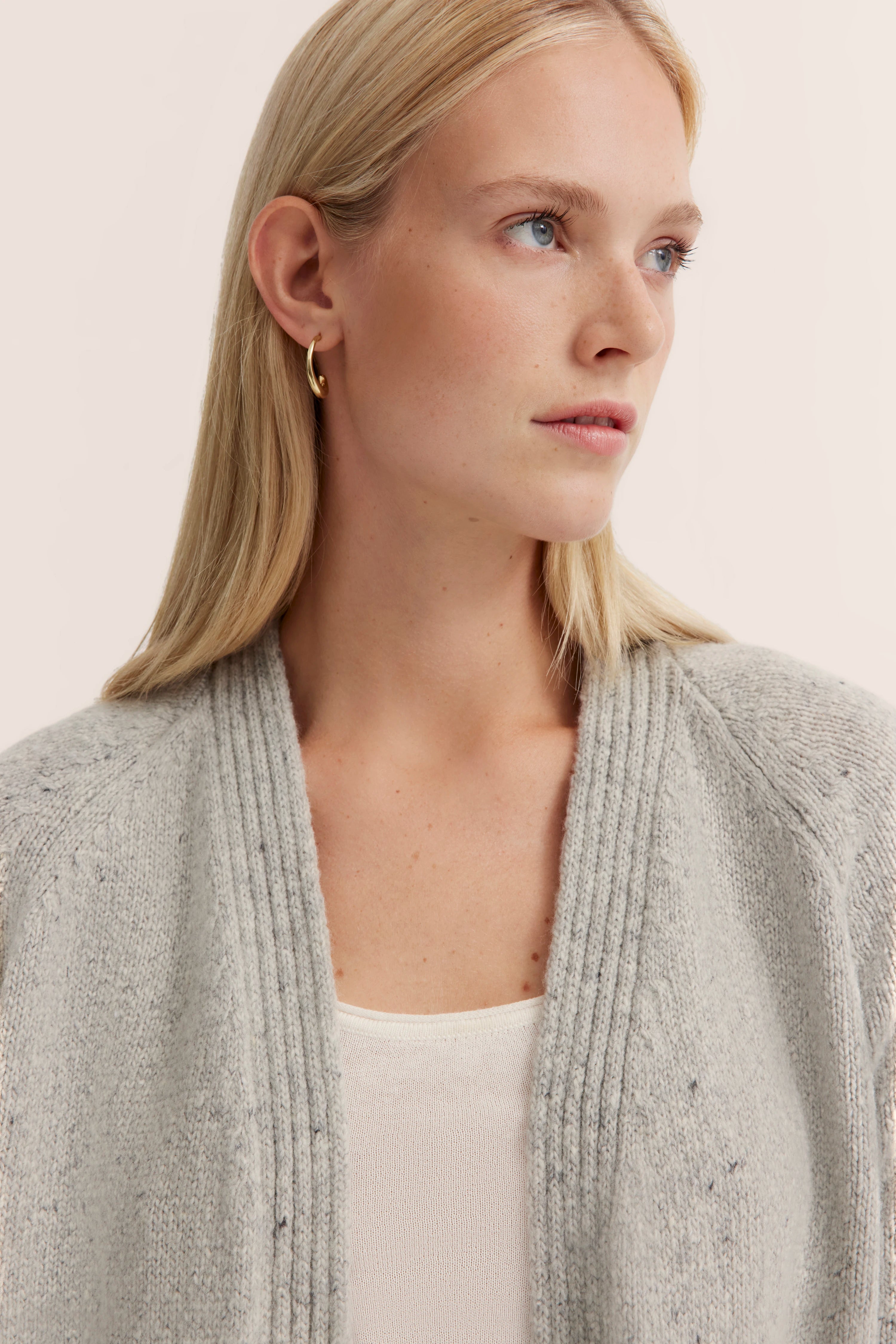 Grauer Strickcardigan über weißem Top, Modelbild, Frau blickt nach rechts, lässige Pose, bugatti Stil.