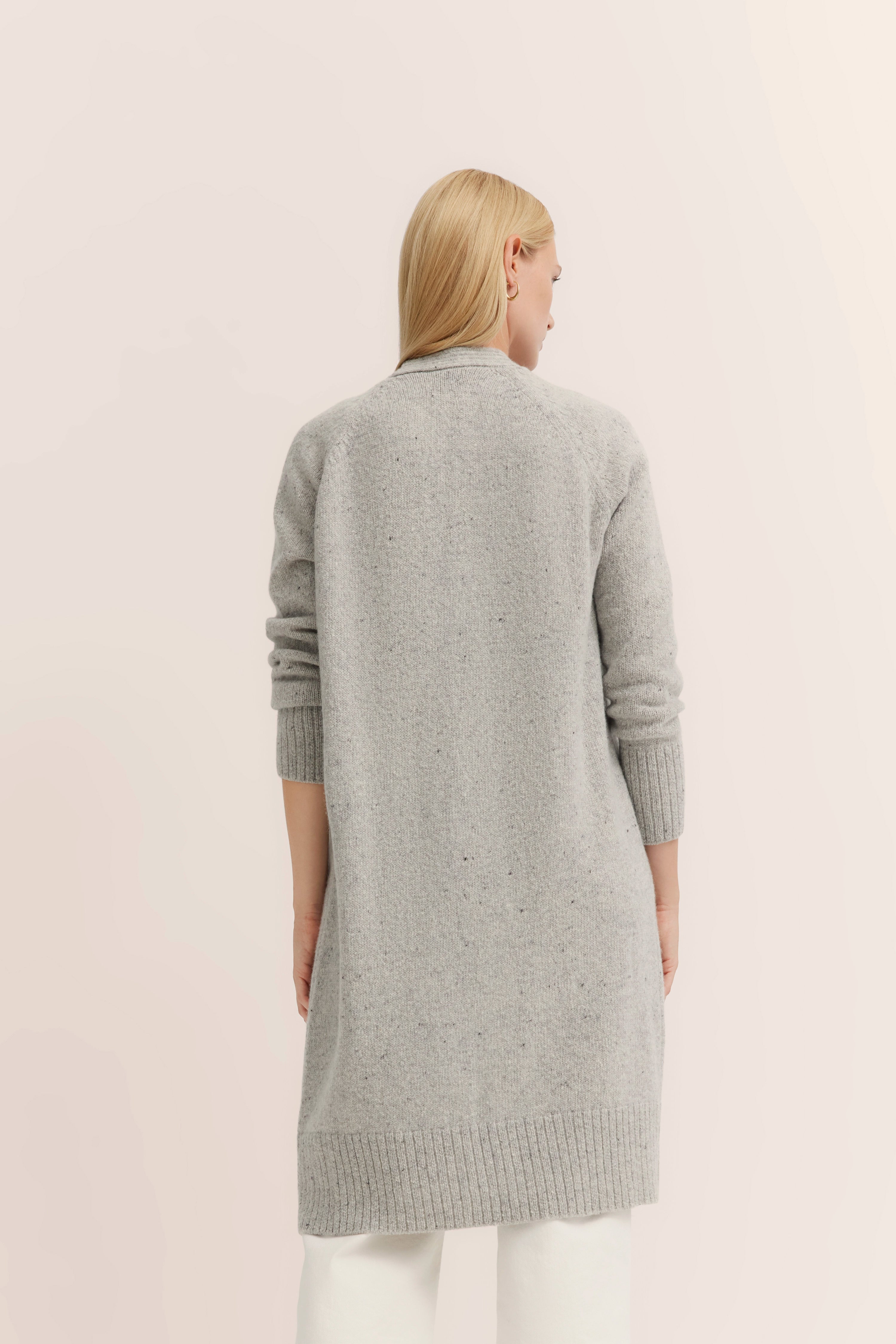 Grauer bugatti Strickmantel, Rückansicht, auf Model, lässige Pose, kombiniert mit weißer Hose.